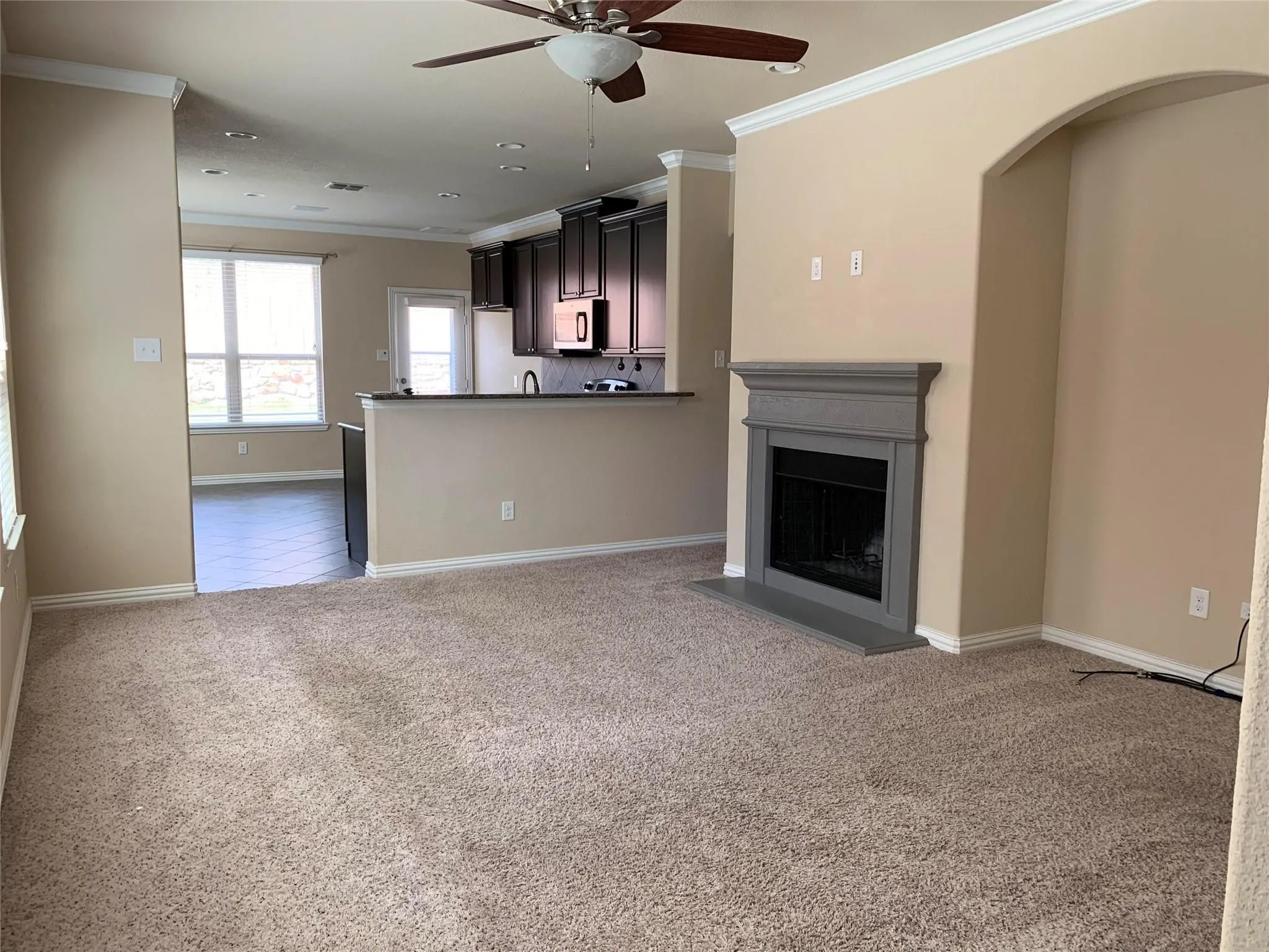 Carpeted living area with a built-in fireplace, a ceiling fan, and crown molding