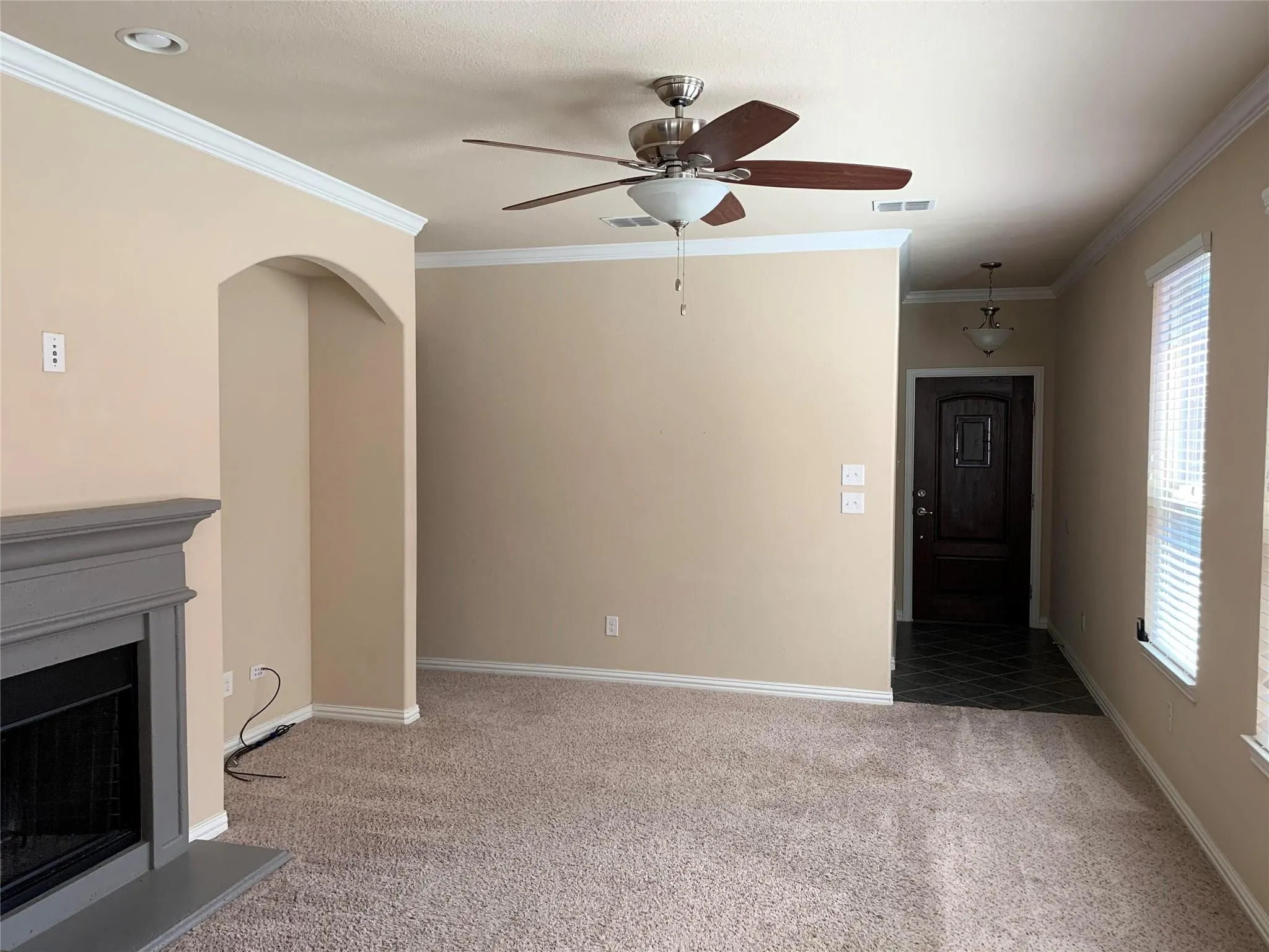 Living area with neutral carpeting and a ceiling fan, featuring a fireplace with a grey mantel and an arched alcove