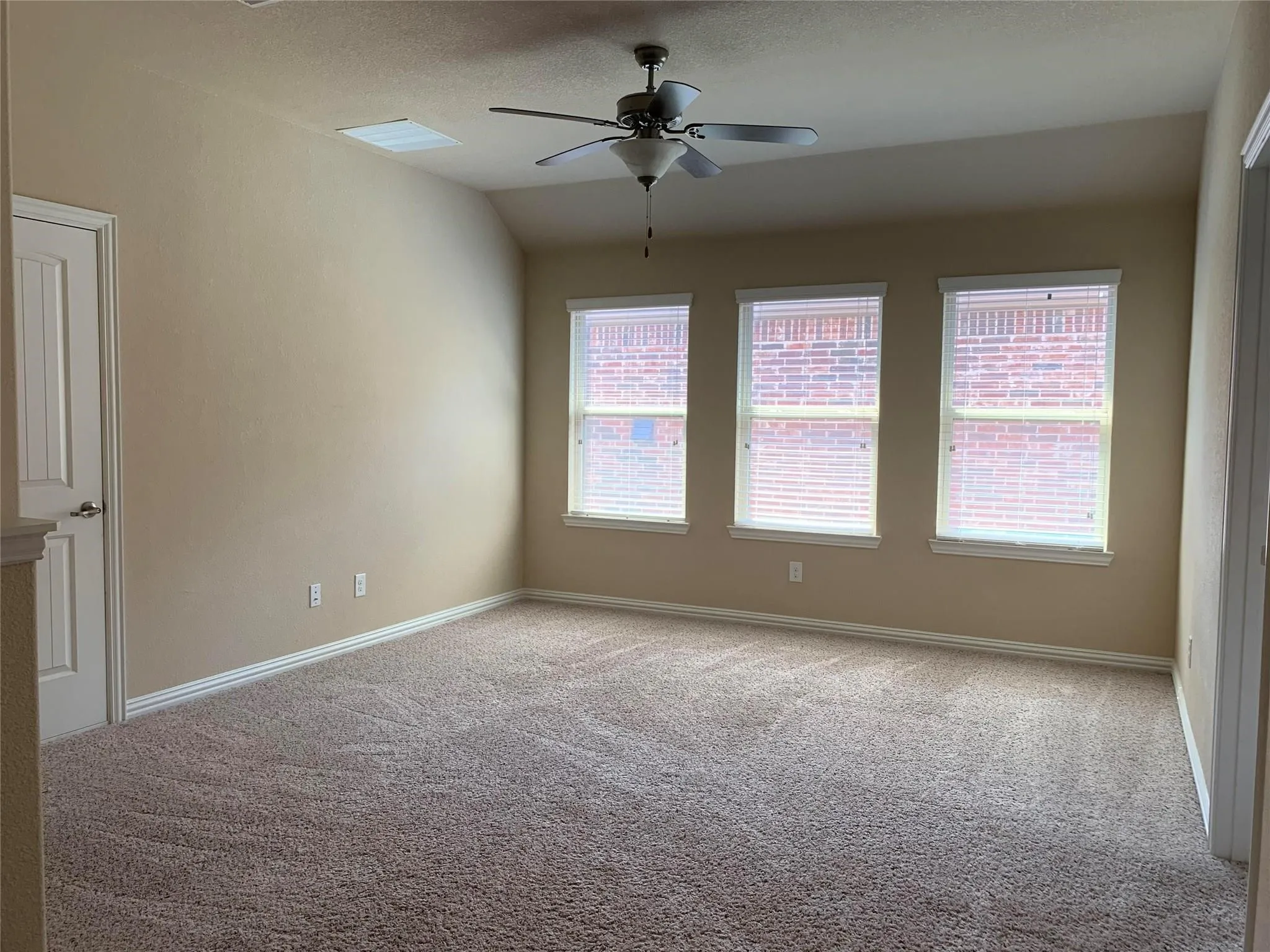 Plush carpeted flooring, three windows with blinds, a ceiling fan, and a paneled door