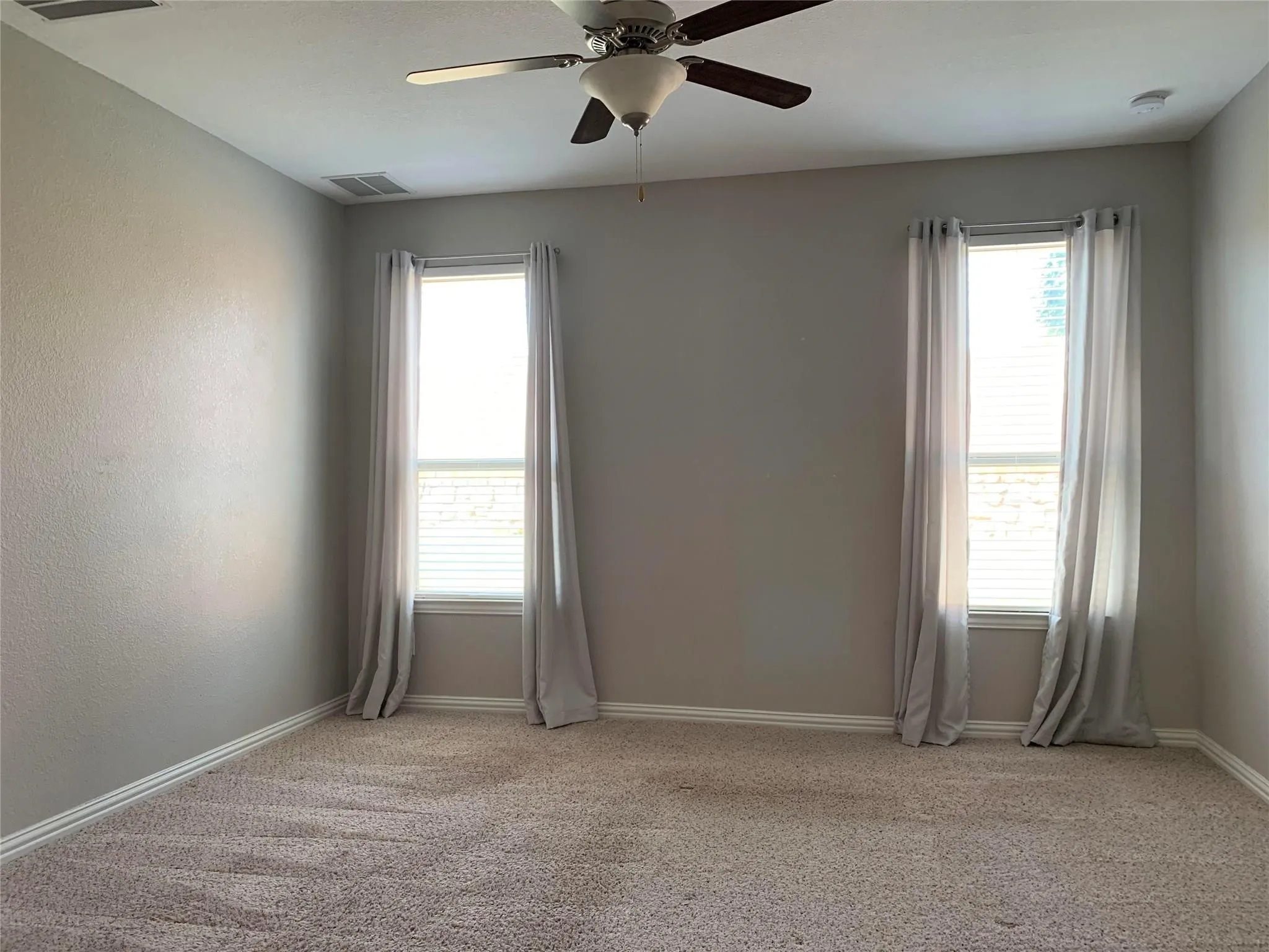 Neutral-toned walls, two windows with blinds, a ceiling fan with light fixture, and plush carpeting