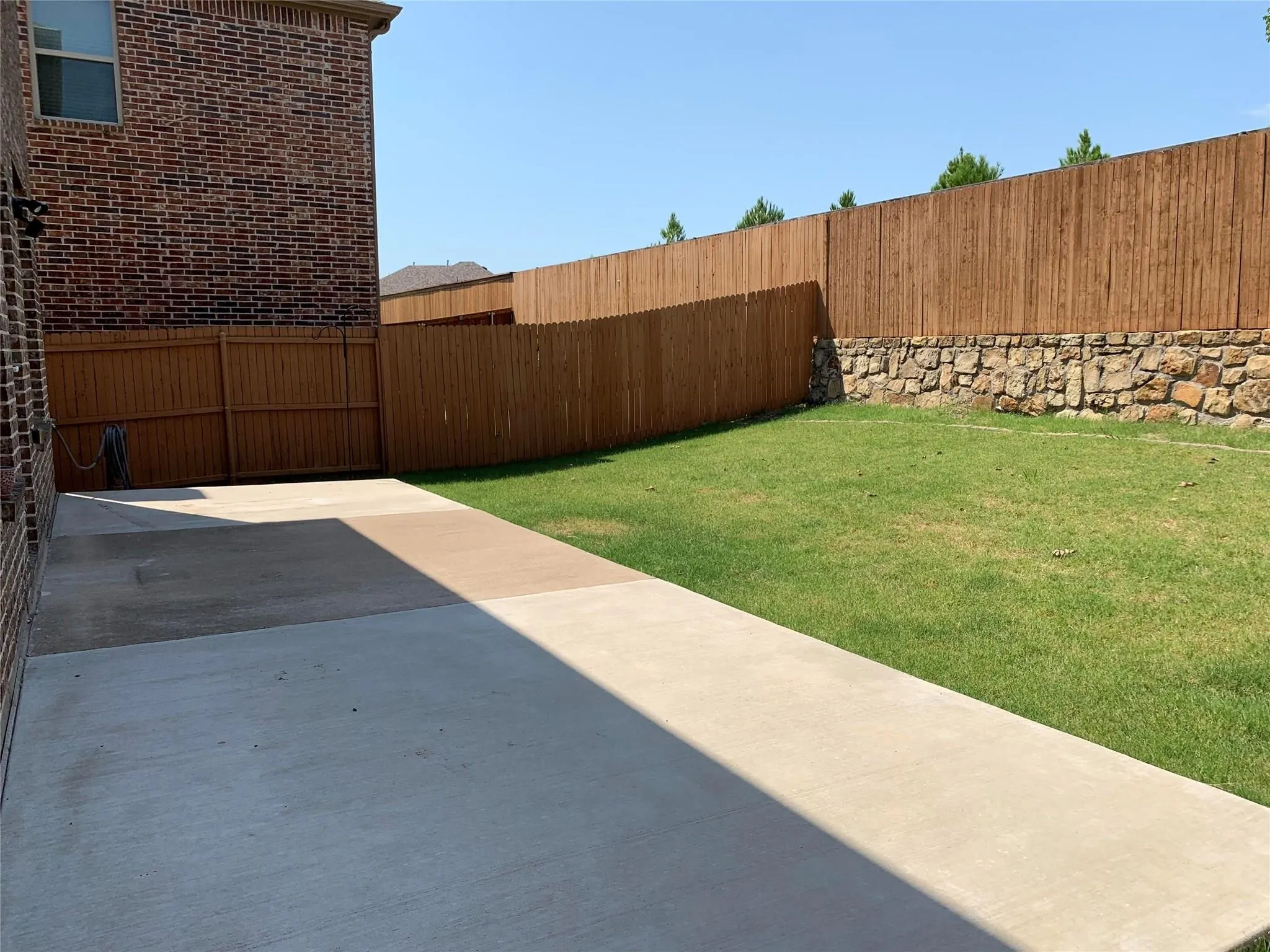 Expansive concrete patio, brick exterior, wood privacy fencing, stone retaining wall, and a grass lawn