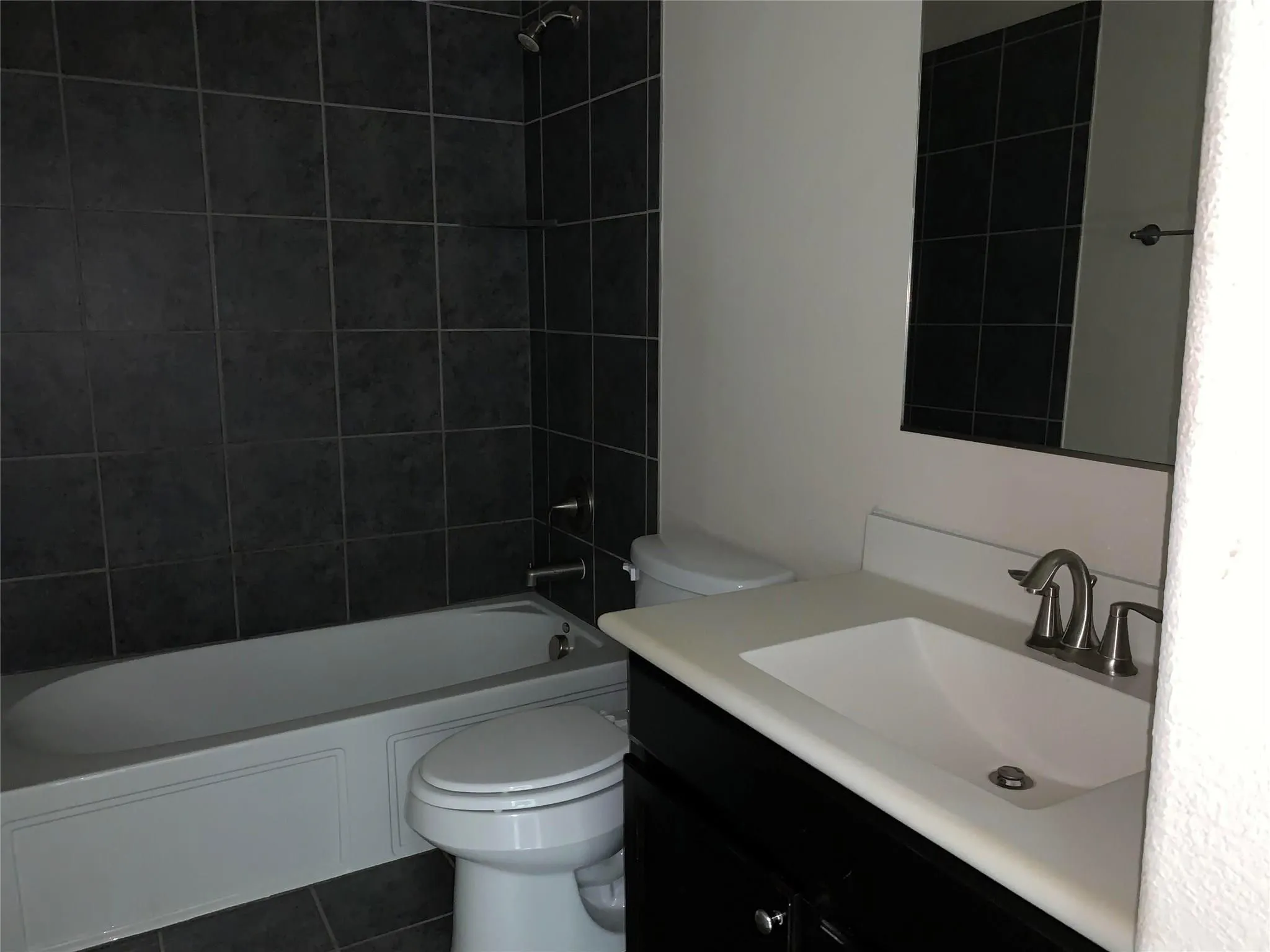 Bathroom featuring dark tiled shower surround, built-in bathtub, dark vanity with integrated sink, and brushed nickel faucet