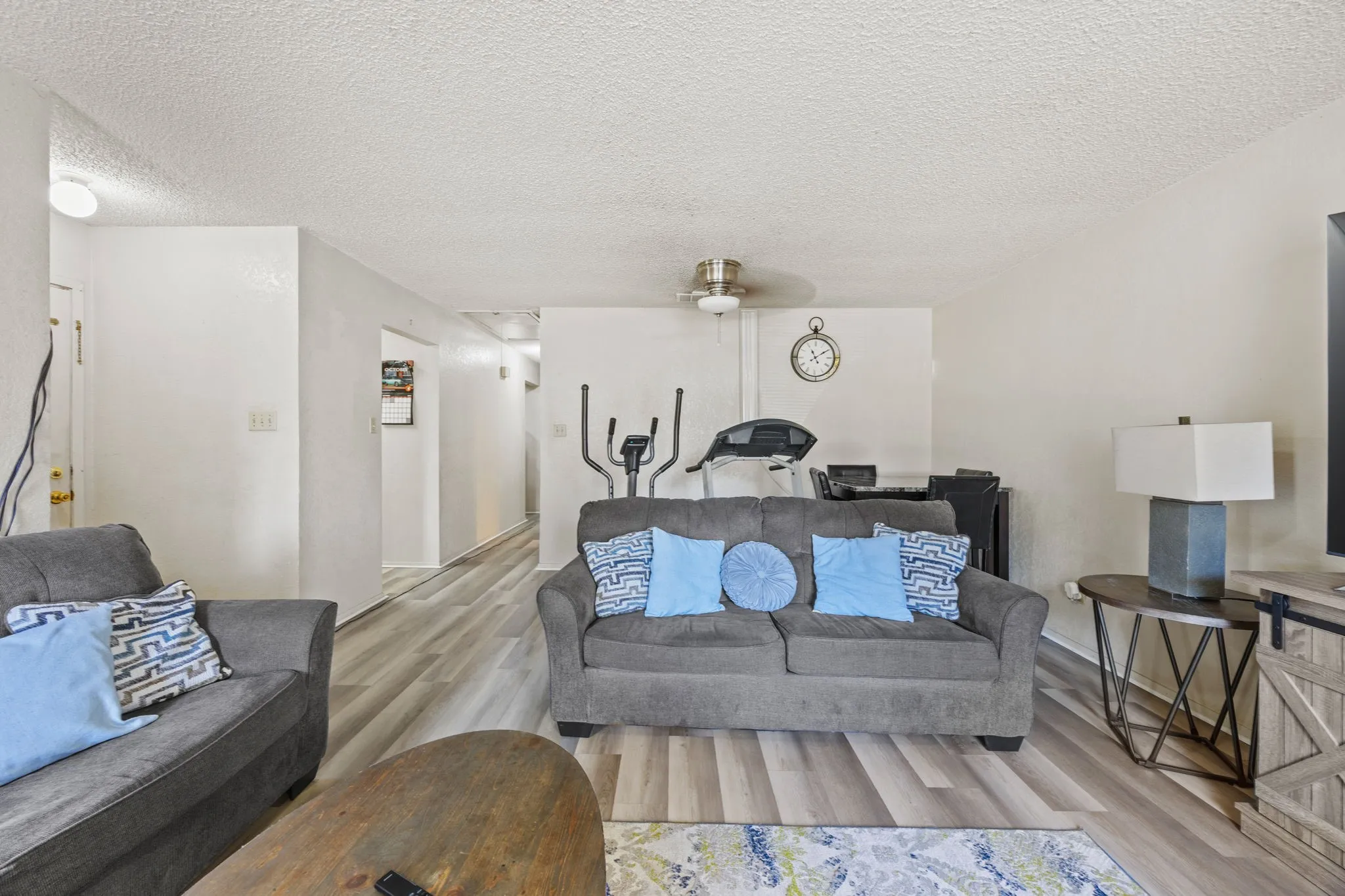 Open-concept living area with wood-finish flooring, textured ceilings, and a ceiling fan