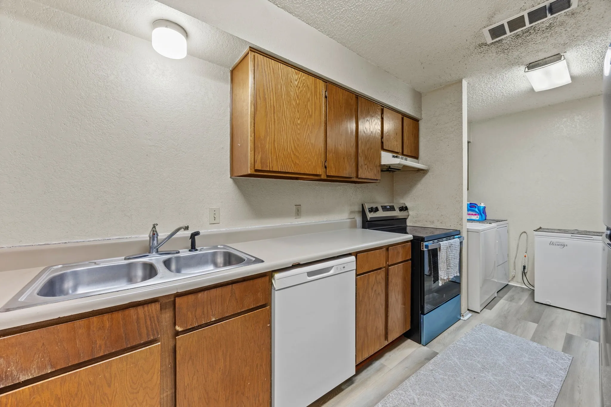Kitchen featuring wood cabinetry, laminate countertops, a double basin stainless steel sink with a chrome faucet, and a built-in dishwasher
