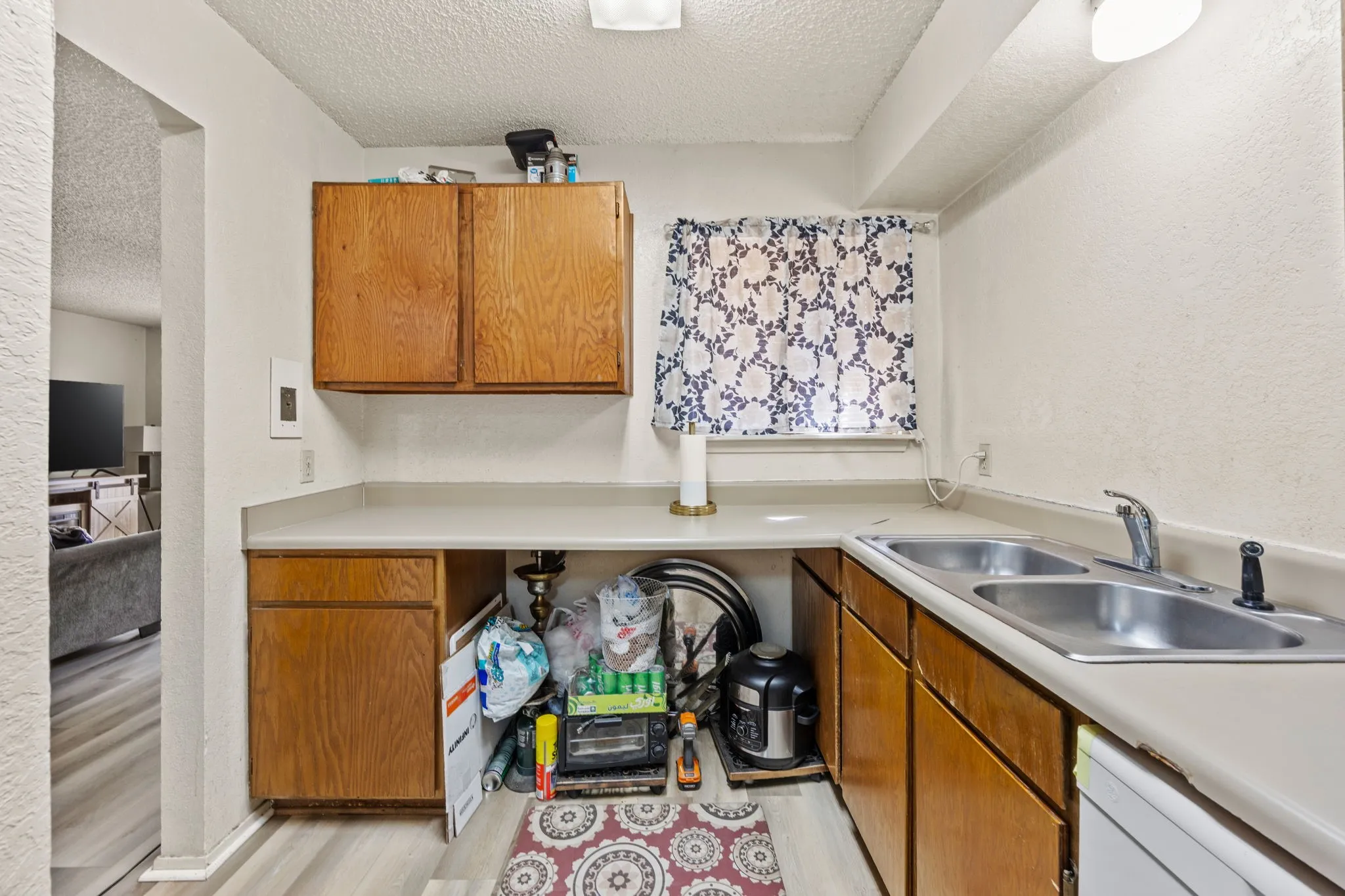 Wood-finish flooring, wood cabinetry, and a double basin stainless steel sink with a chrome faucet