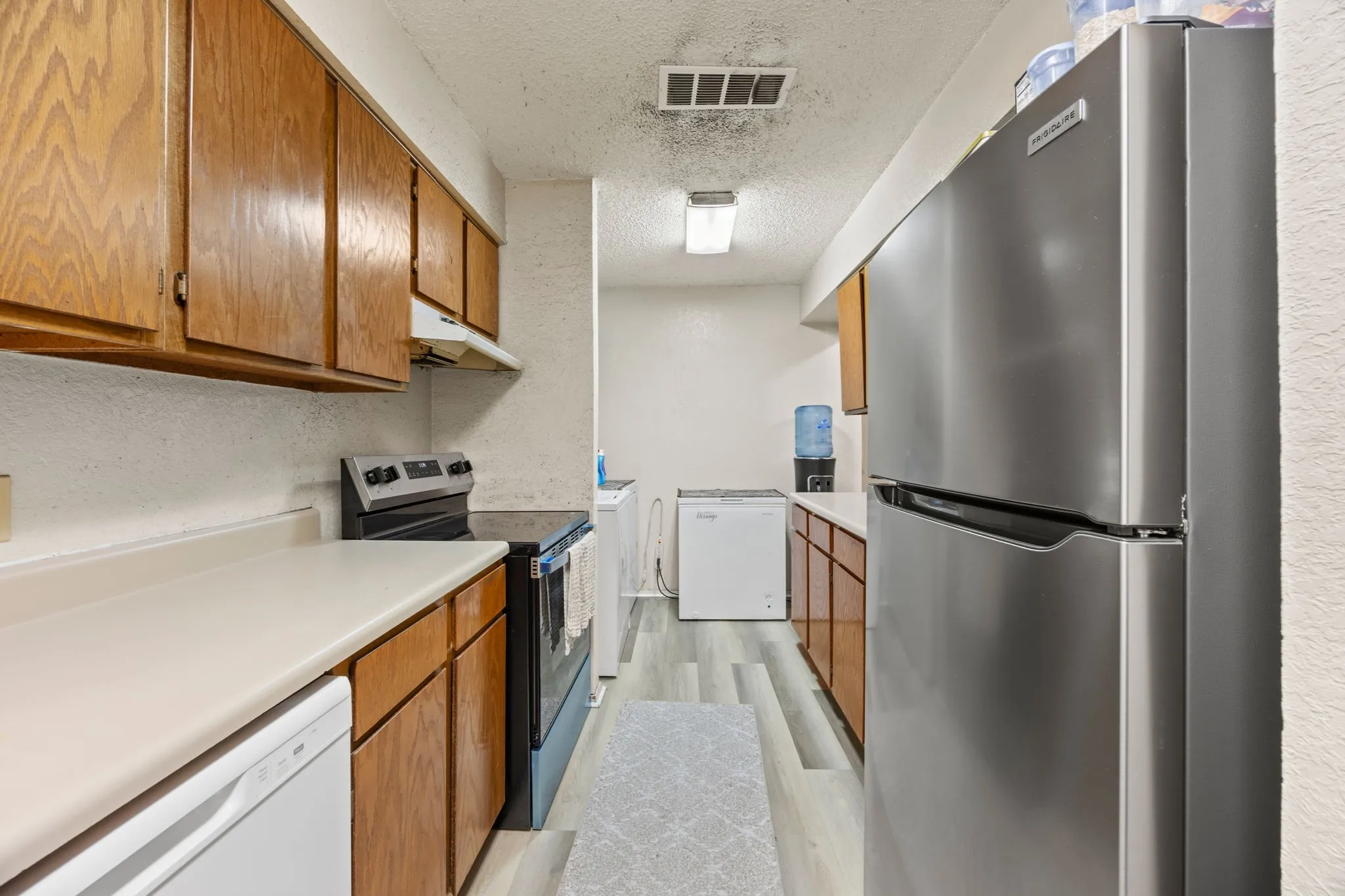 Galley kitchen featuring wood cabinetry, light countertops, stainless steel refrigerator, and wood-finish flooring
