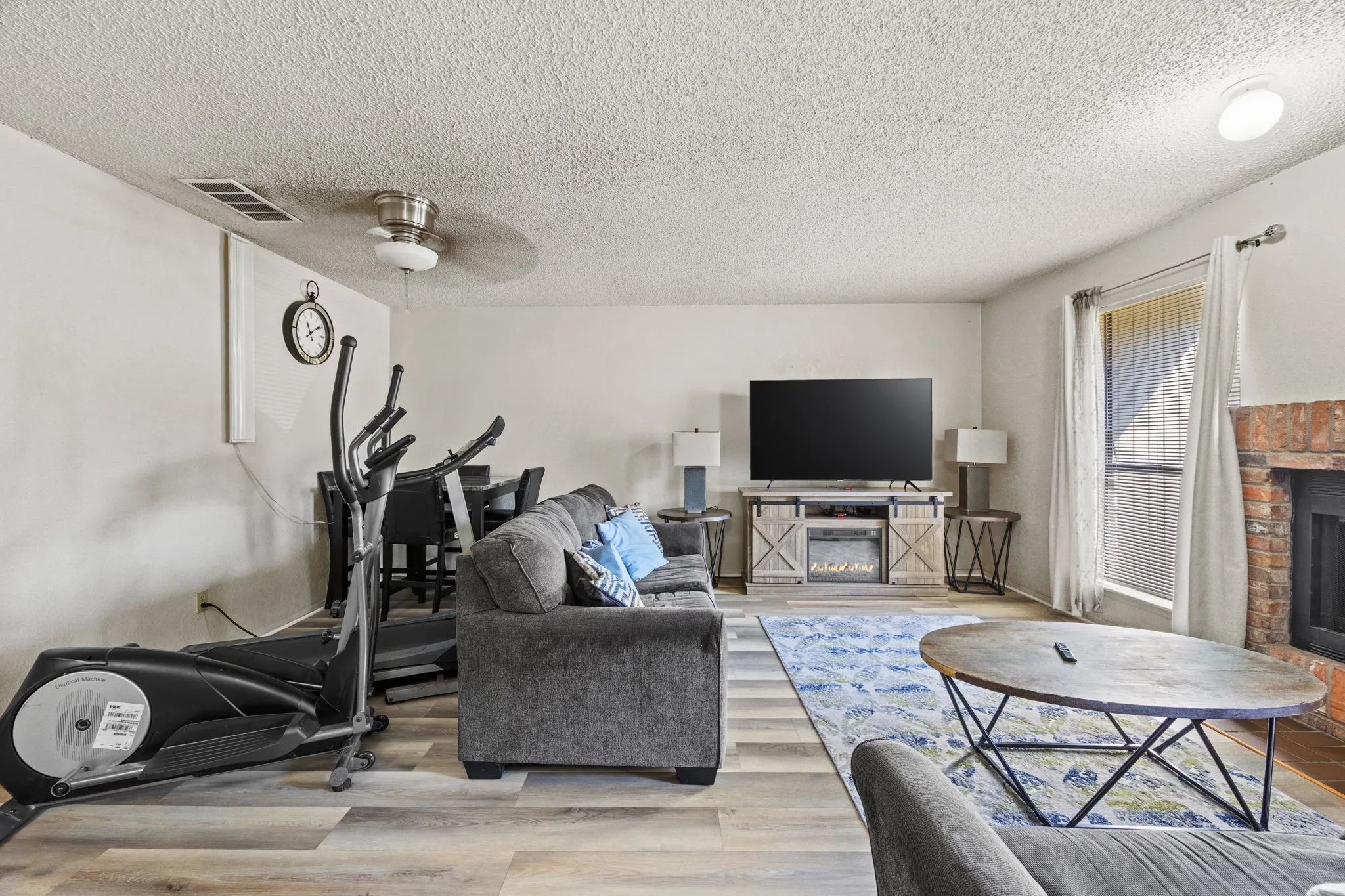Wood-finish flooring, ceiling fan, recessed lighting, brick fireplace, and built-in media console with electric fireplace