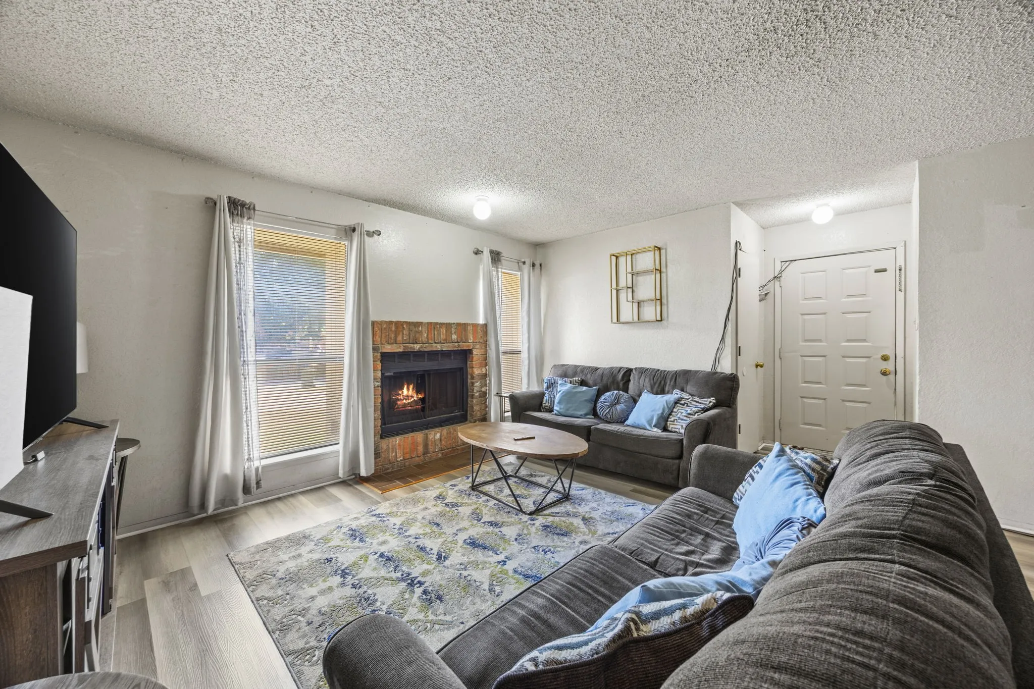 Living area featuring a brick-surround fireplace, light wood-finish flooring, and white paneled entry door