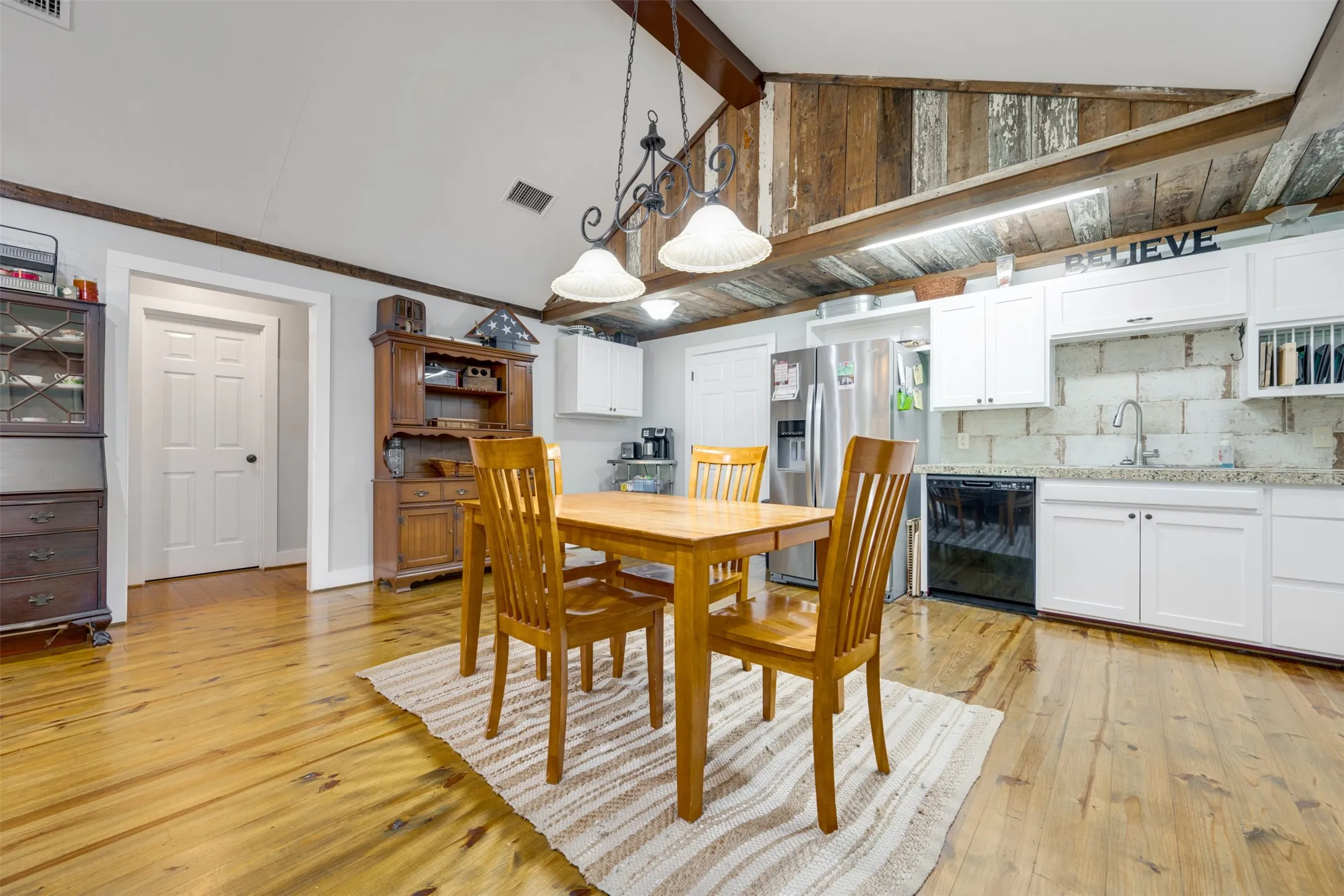 Vaulted ceiling with exposed wood beams, wood-finish flooring, white cabinetry, integrated stainless steel refrigerator, and a built-in dishwasher