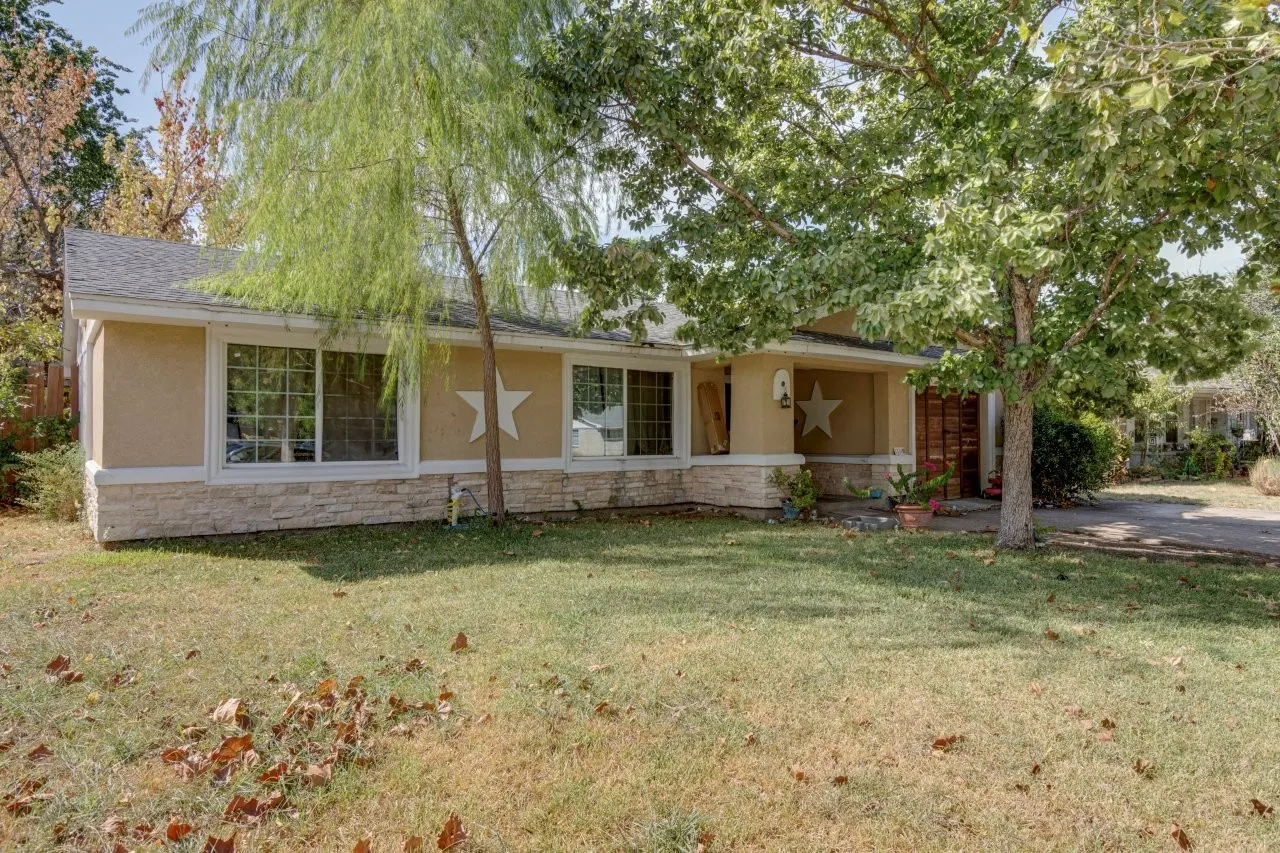 Stucco exterior with stone-finish skirting, prominent front windows, covered entryway, and mature trees