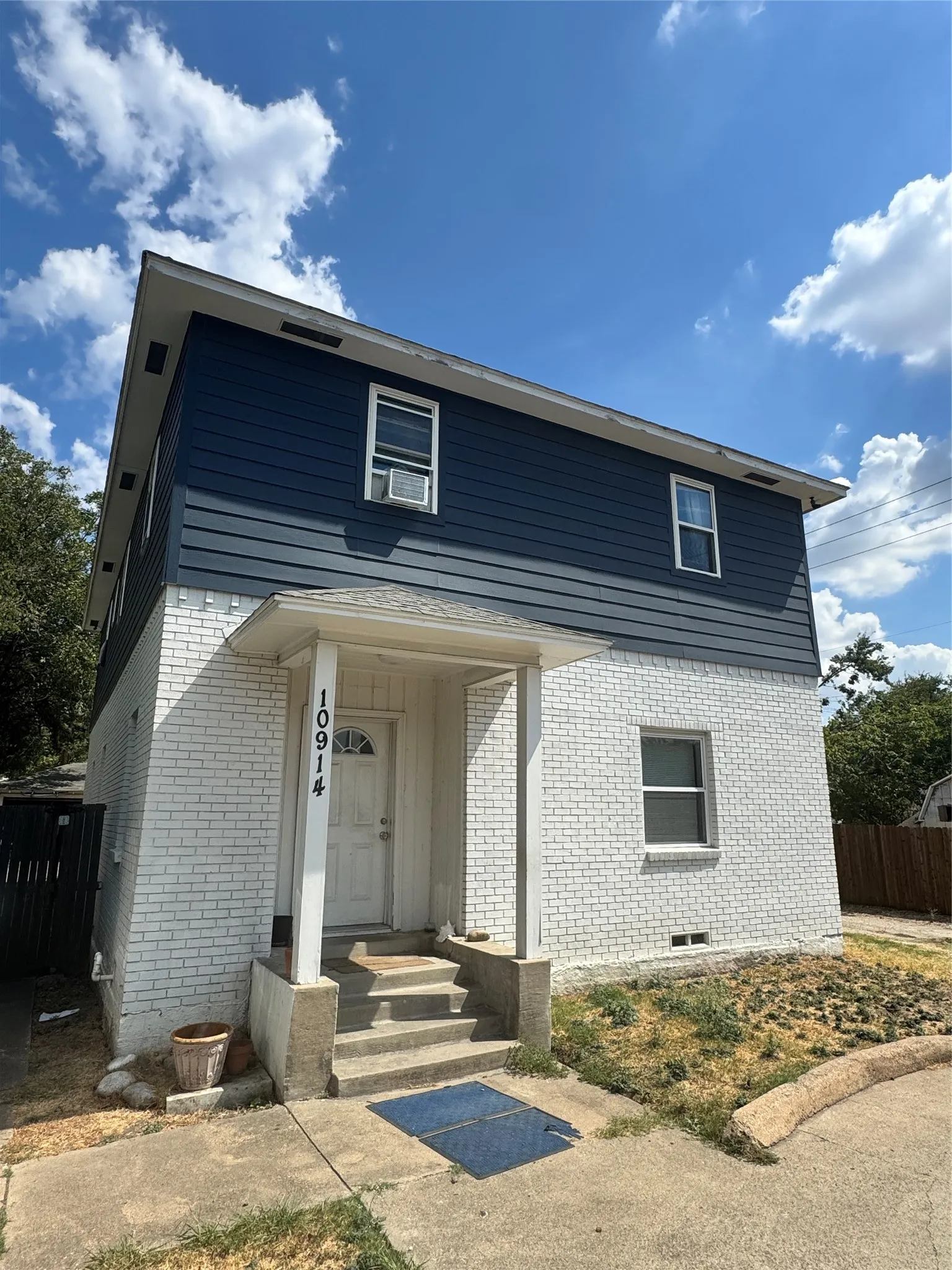 Two-story residence featuring a white brick lower level and blue horizontal siding on the upper level, a covered front porch, and a white entry door