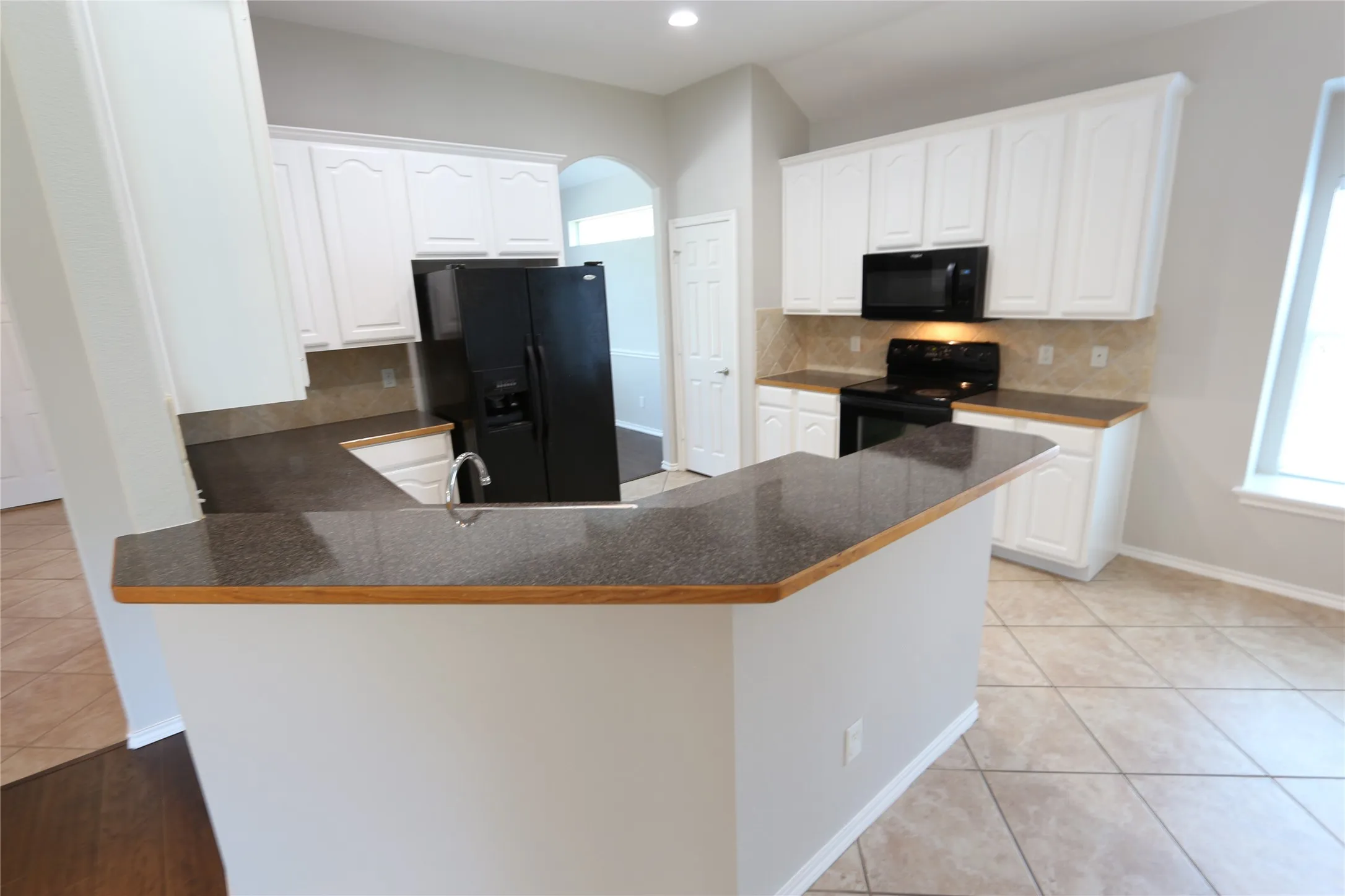 Kitchen with backsplash, white cabinets, black appliances, and light tile floors