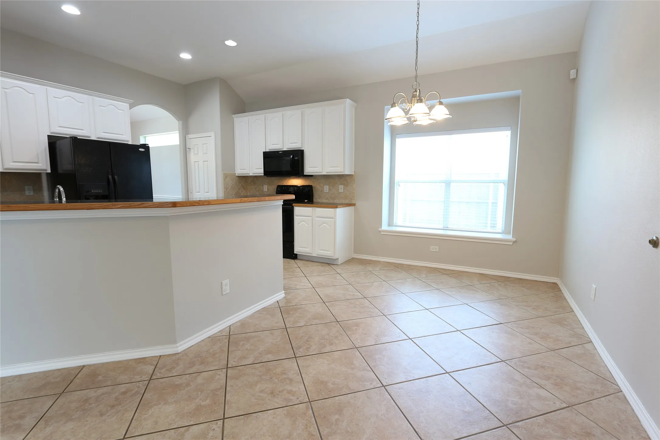 Kitchen with white cabinetry, tasteful backsplash, black appliances, and light tile floors