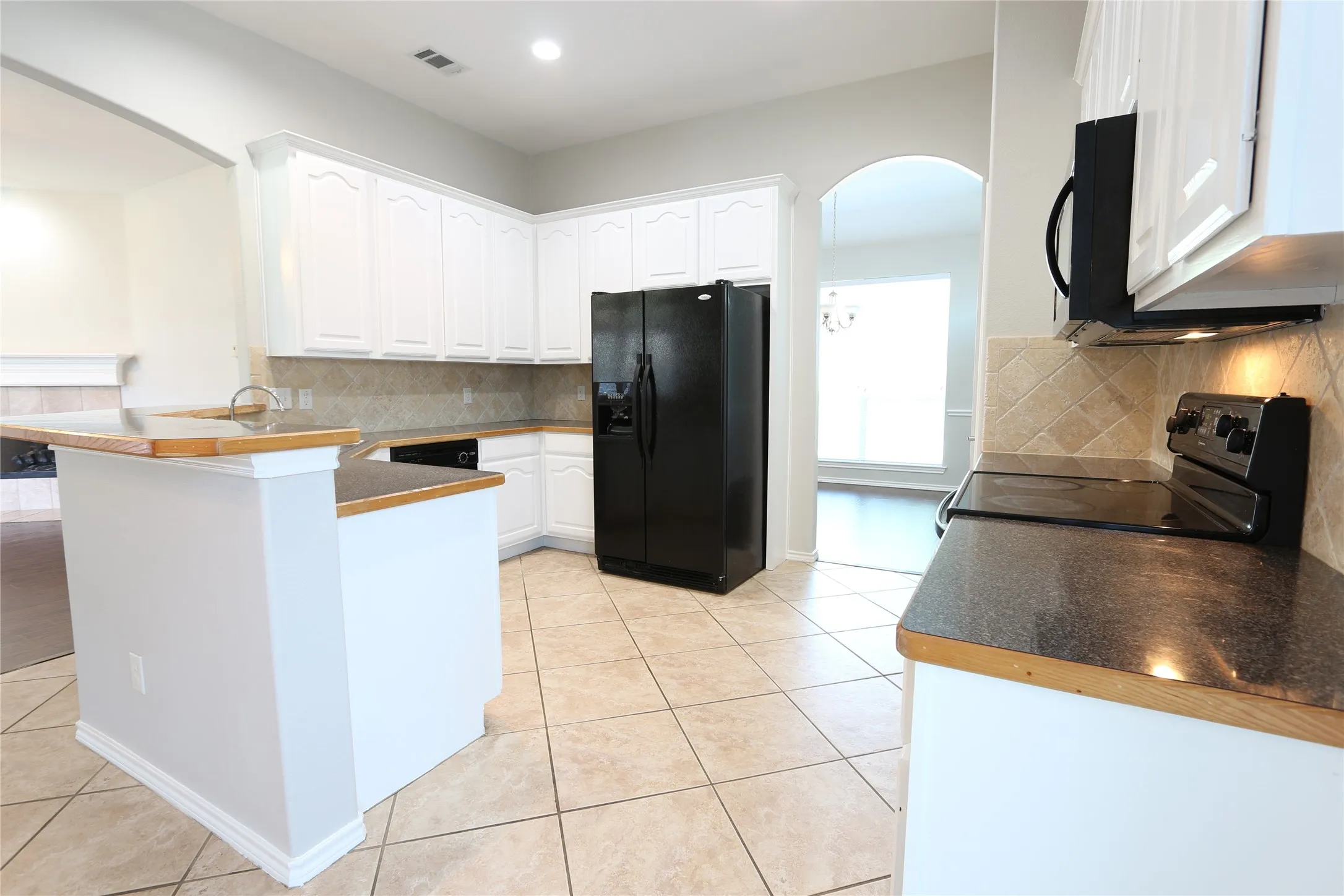 Kitchen featuring white cabinetry, electric stove, black refrigerator with ice dispenser, and tasteful backsplash