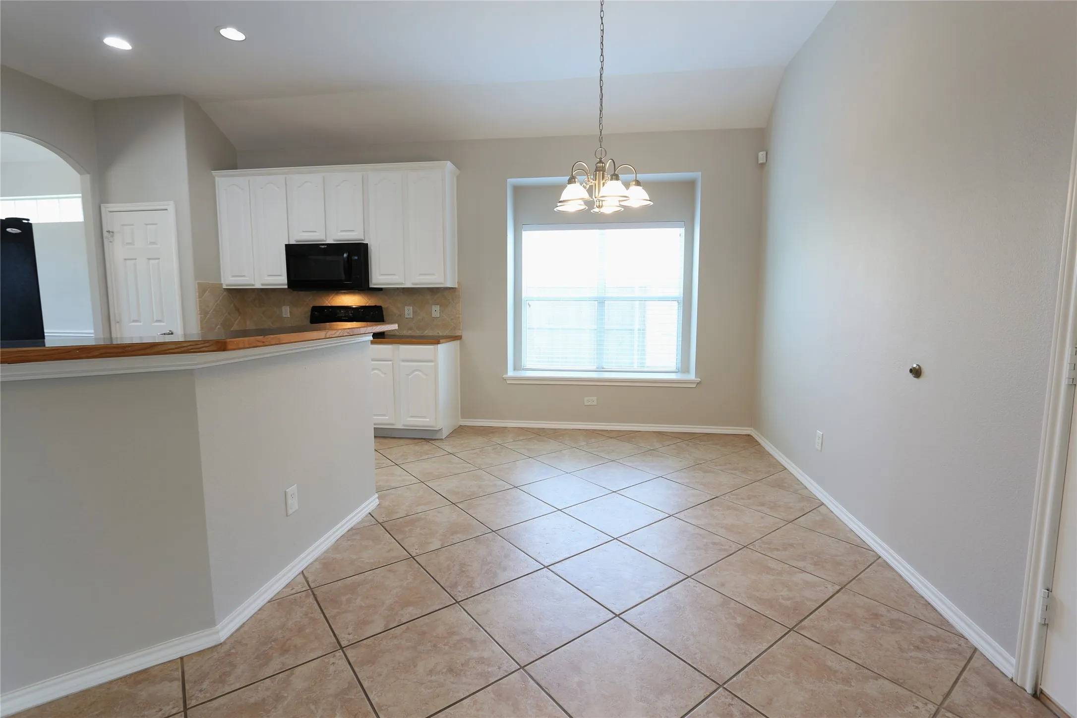 Kitchen with black appliances, hanging light fixtures, backsplash, and white cabinetry