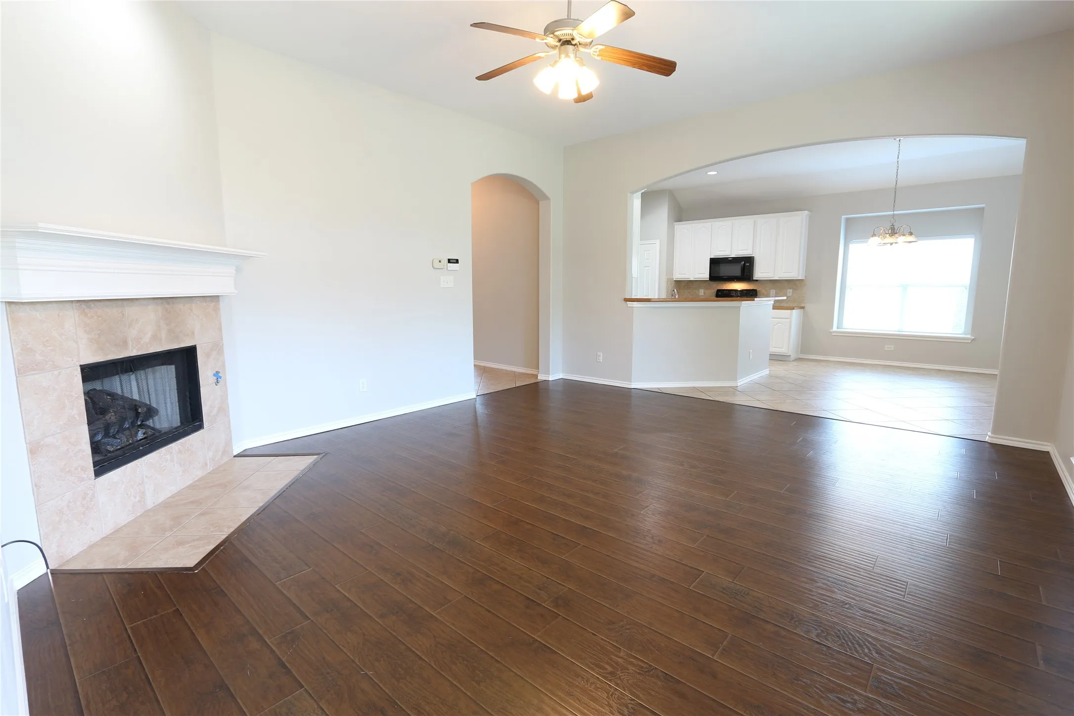 Unfurnished living room featuring ceiling fan with notable chandelier, a fireplace, and wood-type flooring