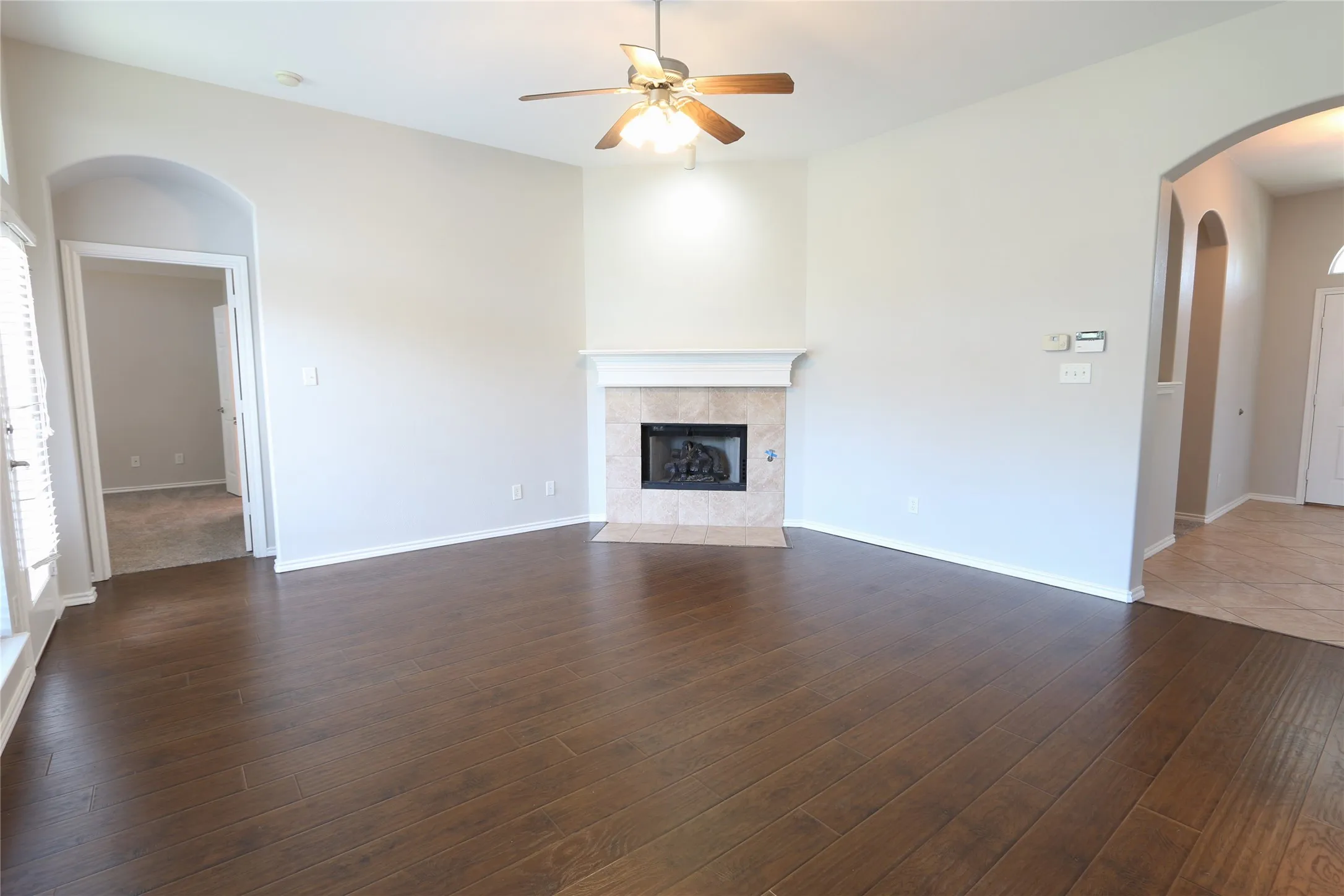 Living room with dark wood flooring, ceiling fan, and a fireplace.