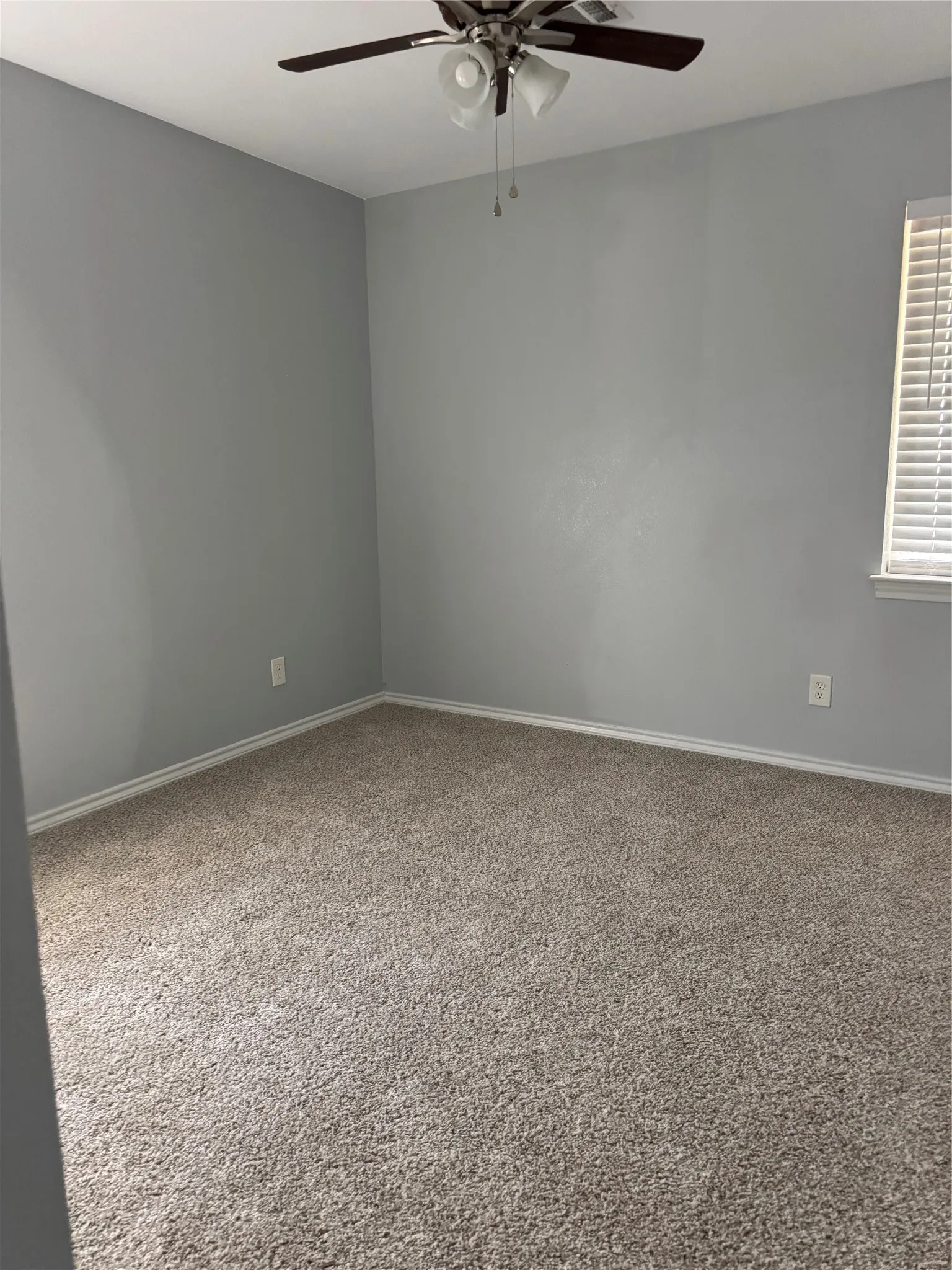 Neutral gray walls, light-colored carpeting, and a ceiling fan with integrated lighting