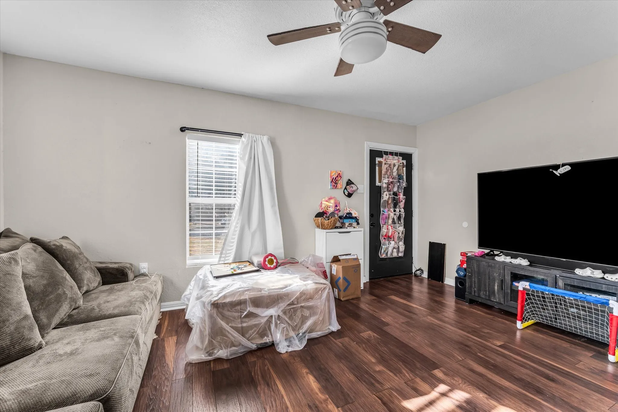 Wood-finish flooring, ceiling fan with integrated lighting, natural light from the window, and a solid-panel door