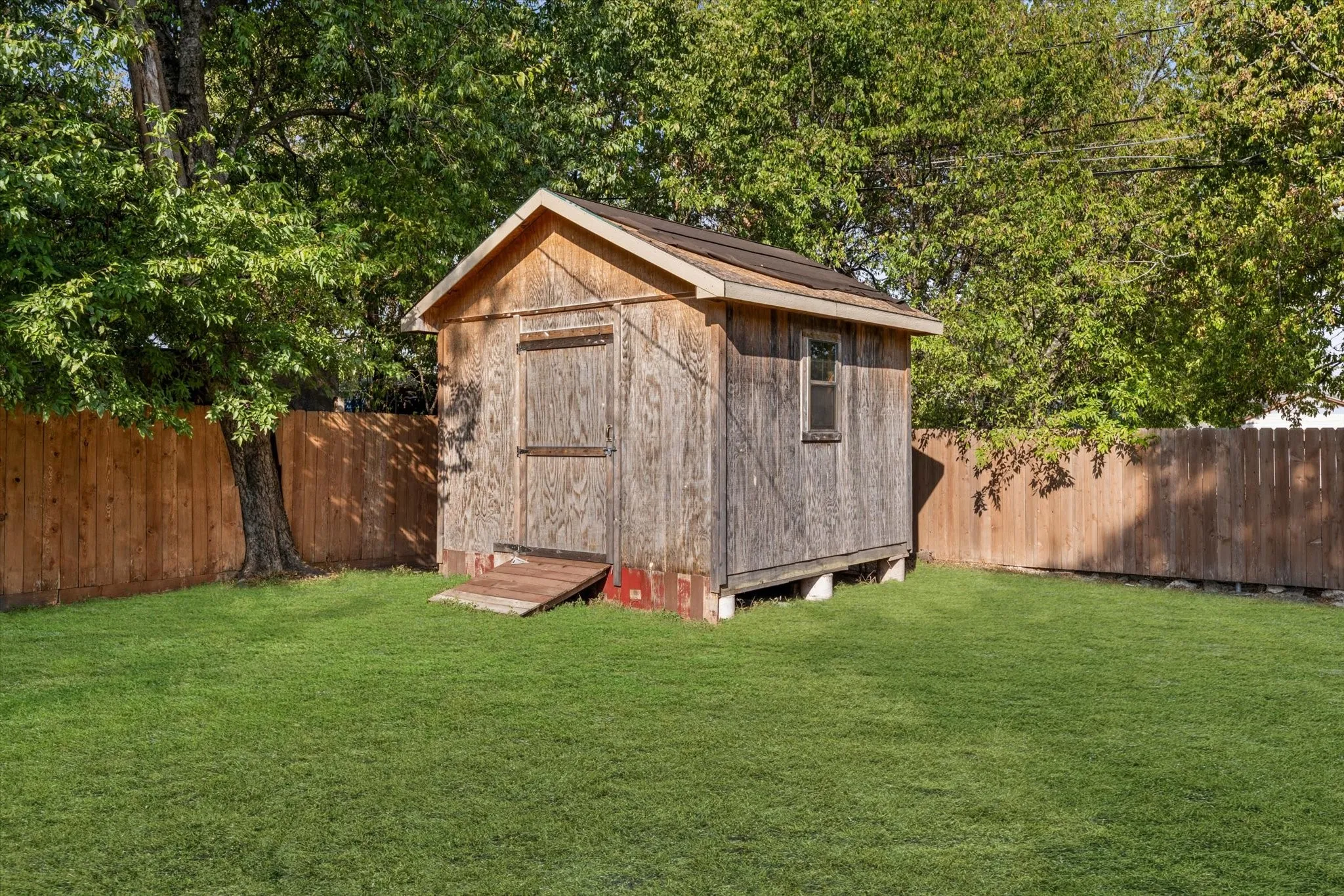Expansive green lawn featuring a wooden storage shed with a window and solid wood fencing
