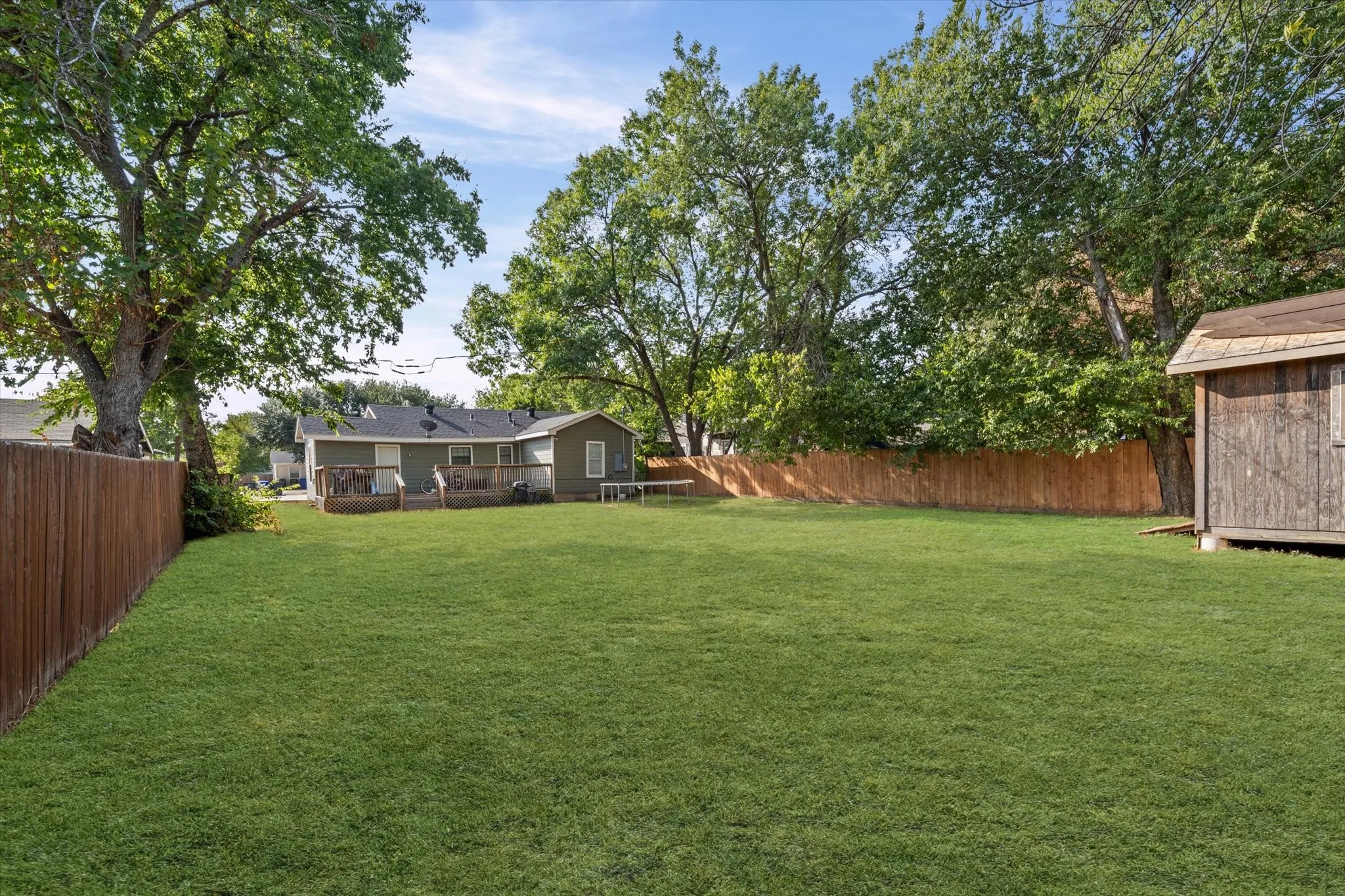 Spacious fenced backyard featuring a wood privacy fence, mature trees, a detached storage shed, and a rear deck
