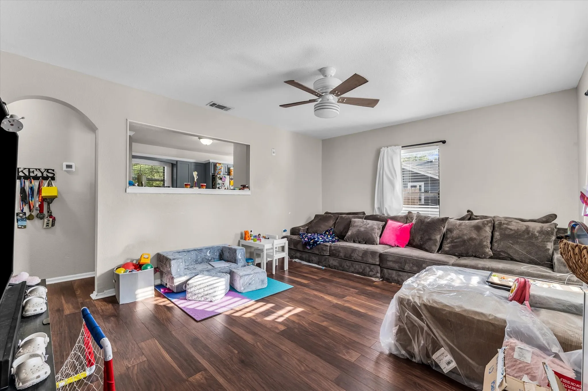Wood-finish flooring throughout, ceiling fan with light fixture, arched doorway, and built-in wall pass-through