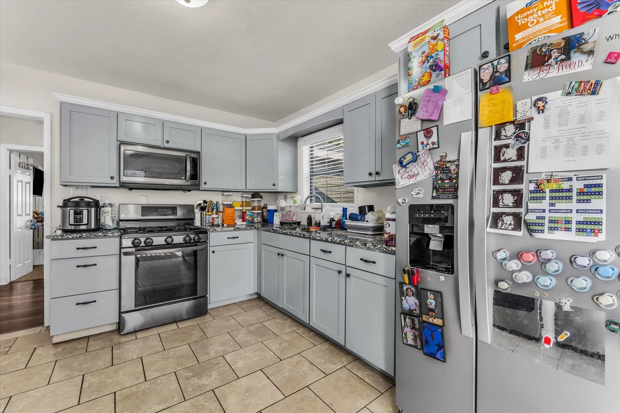 Kitchen featuring tile flooring, light gray cabinetry, stainless steel appliances, and dark countertops