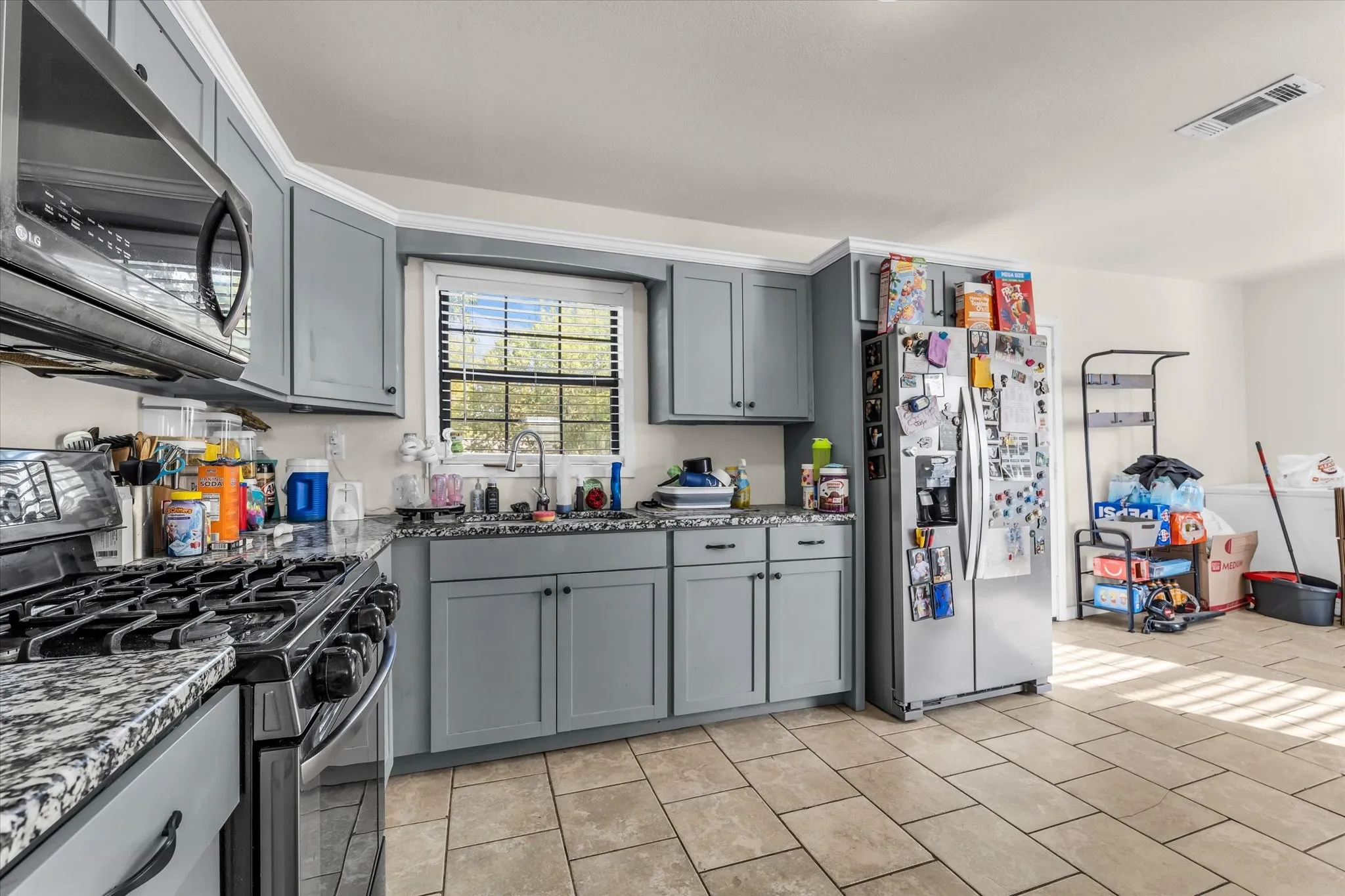Kitchen featuring light gray cabinetry, dark speckled countertops, stainless steel appliances, and a window above the sink