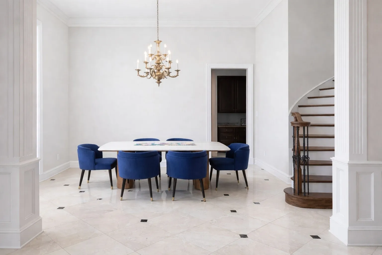 This room features light-colored tile flooring with dark square inlays, a grand chandelier, and a curved wooden staircase with dark metal railings