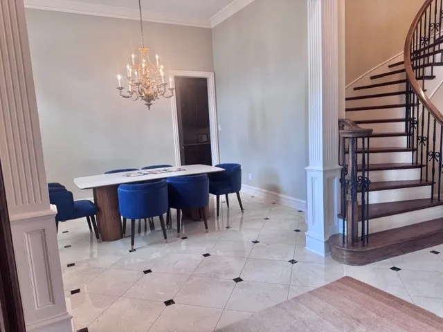 This space features light-toned tiled flooring with dark square accents, crown molding, and a chandelier