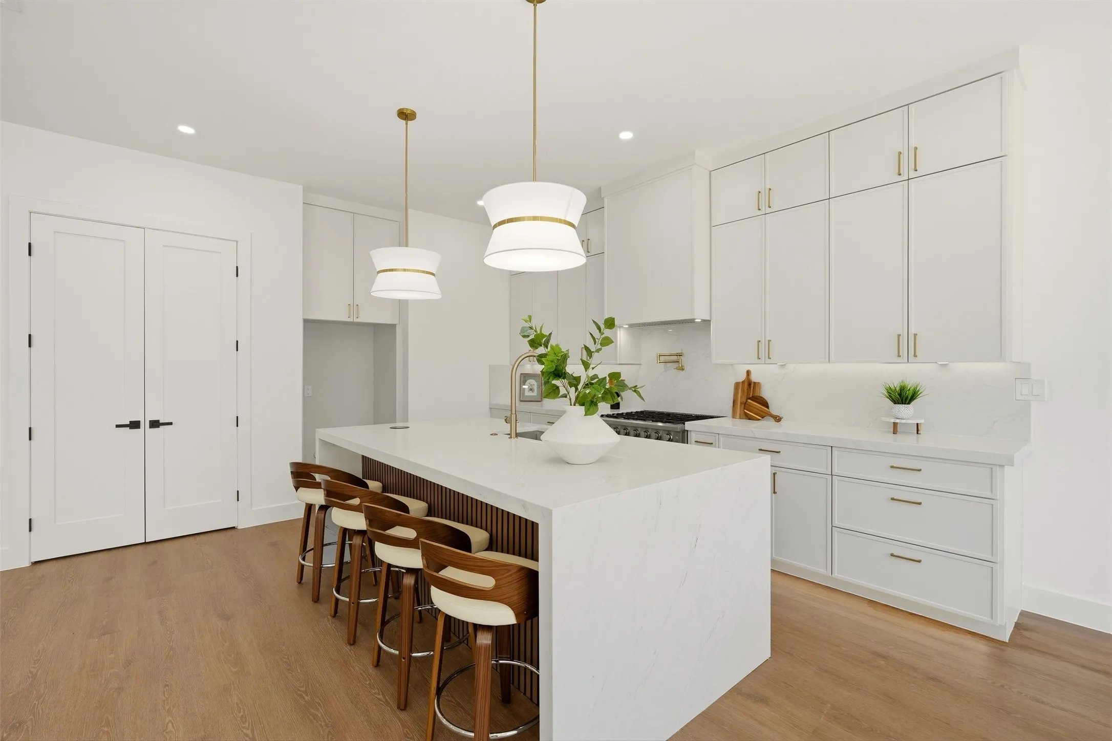 Central kitchen island with a waterfall countertop, brass hardware, wood-finish flooring, and white cabinetry