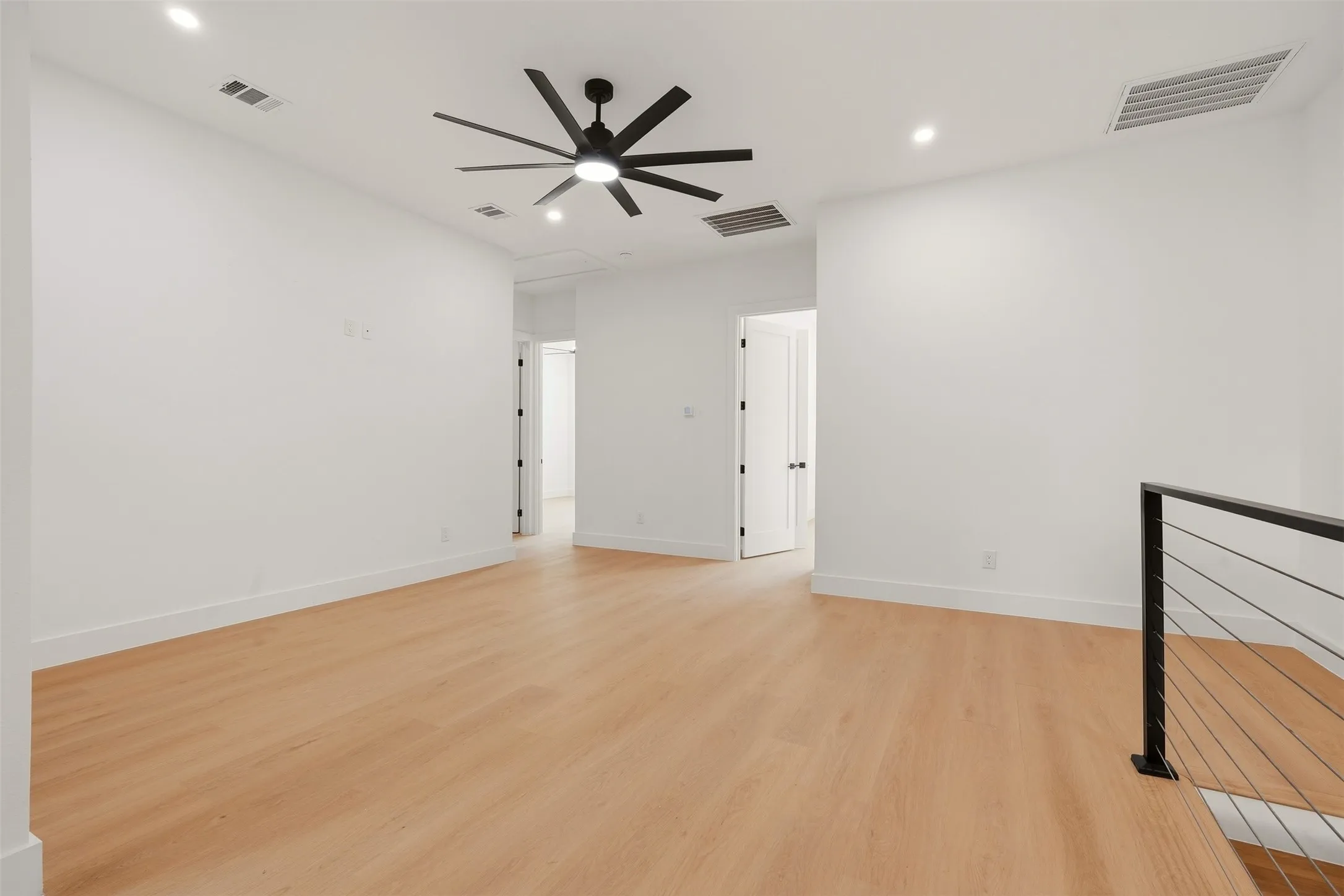 Wood-finish flooring, recessed lighting, ceiling fan, white walls, and modern metal railing
