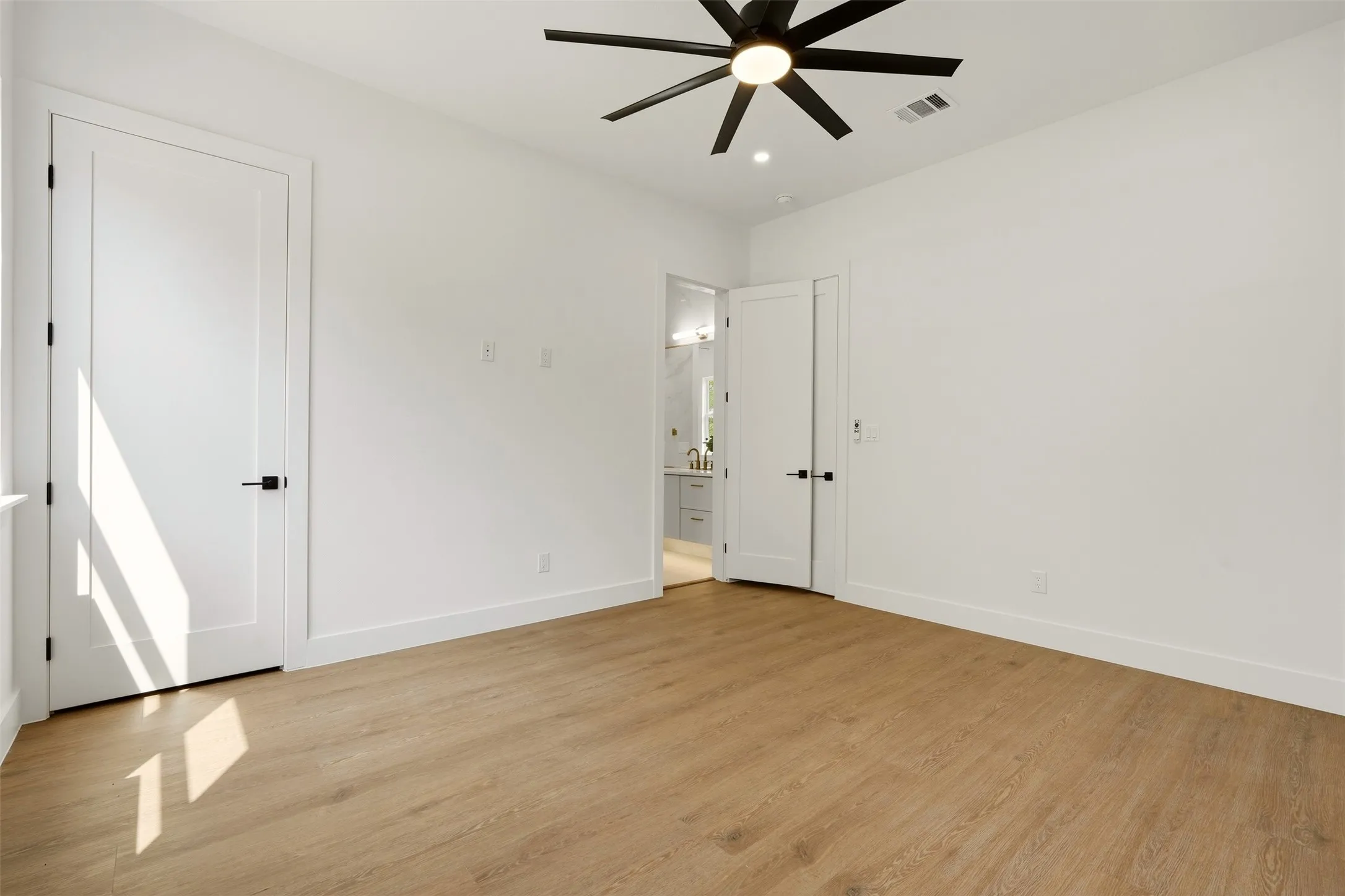 Wood-finish flooring, crisp white walls, contemporary ceiling fan, modern interior doors with matte black hardware, and bright recessed lighting