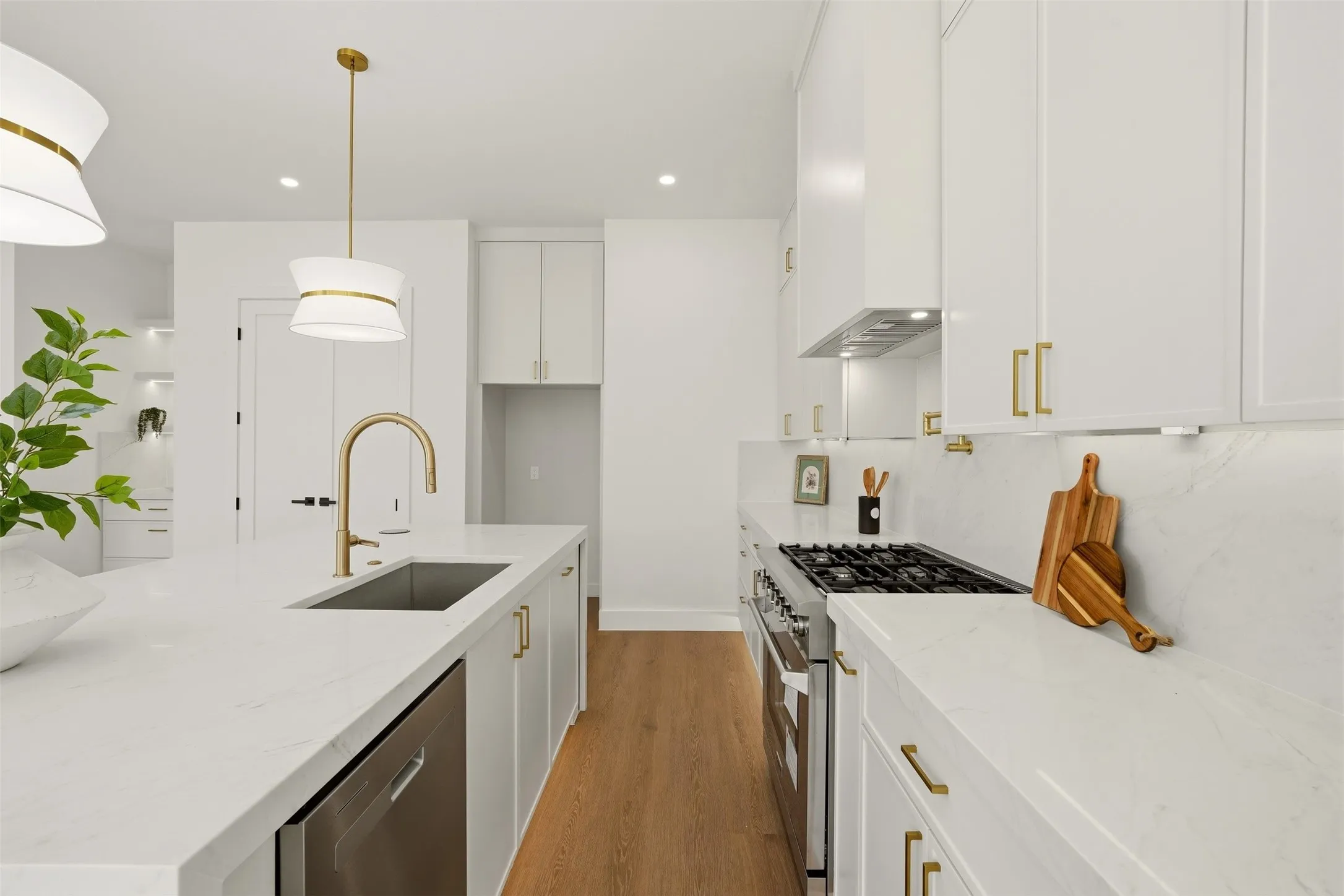 White shaker cabinetry with gold-tone hardware, stainless steel appliances, a kitchen island with an undermount sink, and wood-finish flooring
