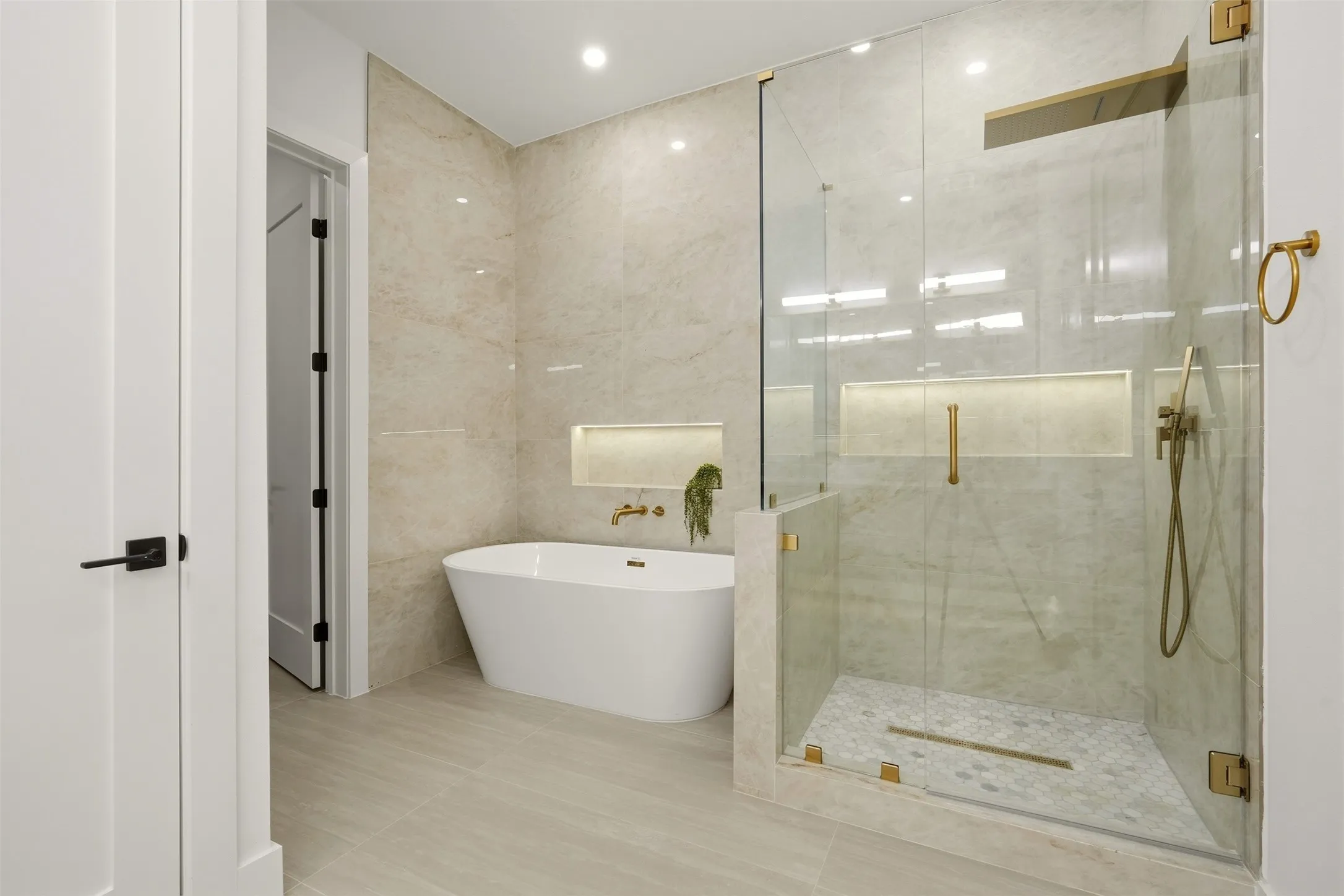 Freestanding soaking tub, walk-in shower with glass enclosure, gold-finish fixtures, and light-toned tile flooring
