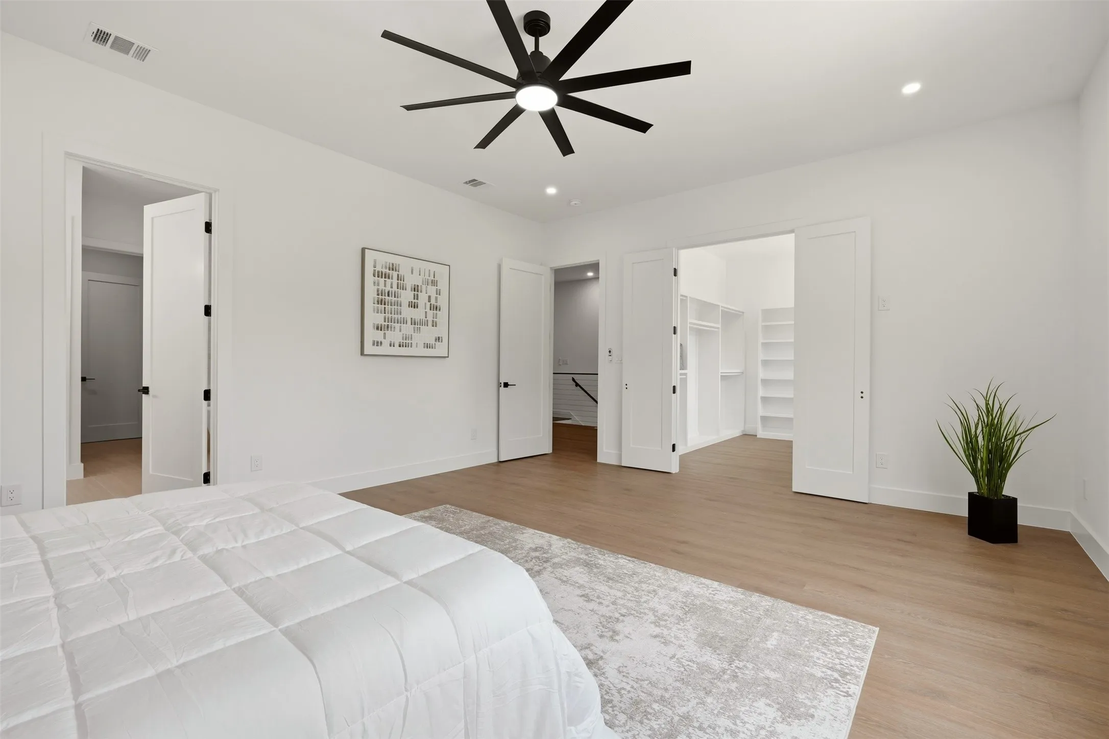 Spacious room featuring wood-finish flooring, a modern black ceiling fan, recessed lighting, and a built-in walk-in closet with shelving