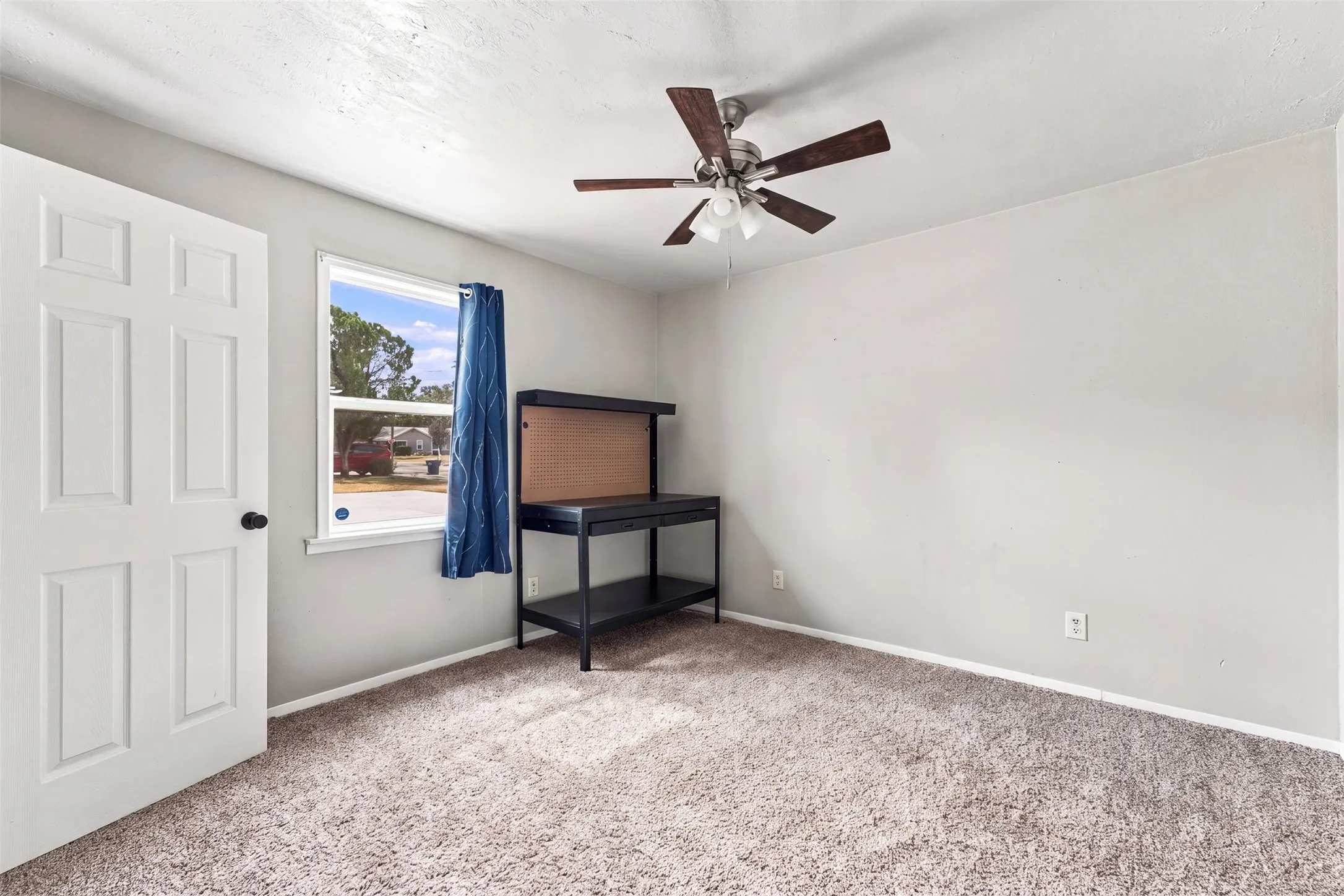 Plush carpeted flooring, window with exterior scenery, ceiling fan with light kit, and a white panel door with black hardware