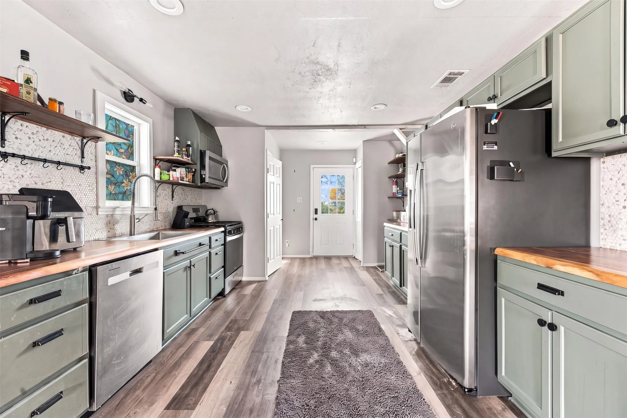 Kitchen featuring wood-finish countertops, stainless steel appliances, light-toned cabinetry, and a textured backsplash