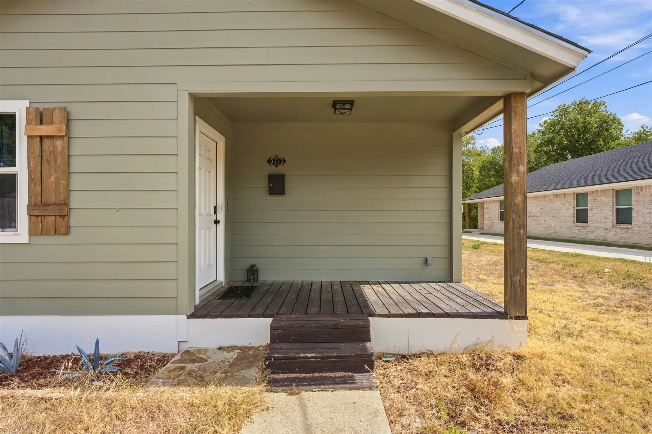 Covered front porch with wood-finish decking, light green siding, and a white entry door