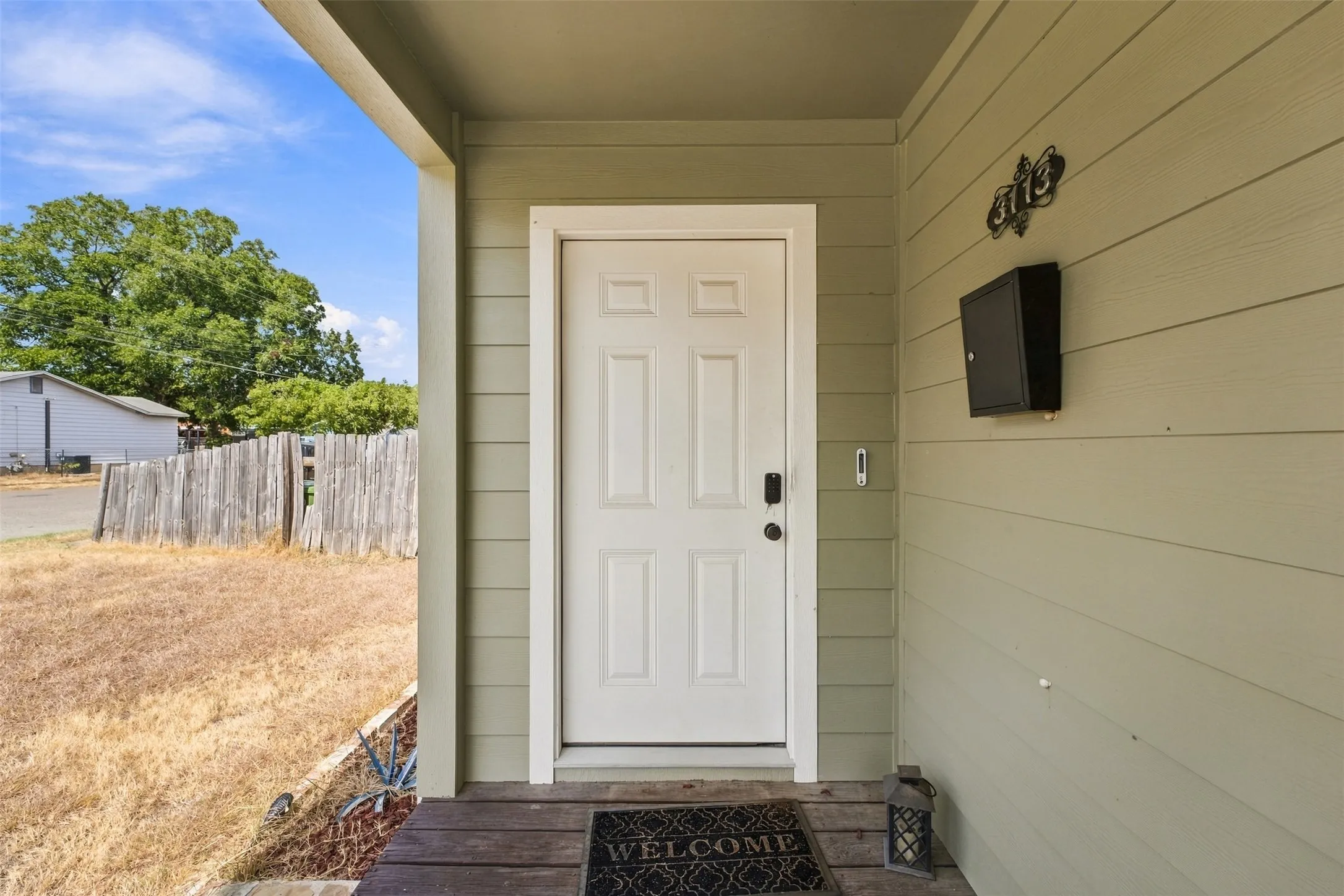 Covered porch entry featuring a paneled door with smart lock, exterior wall siding, and mounted mailbox