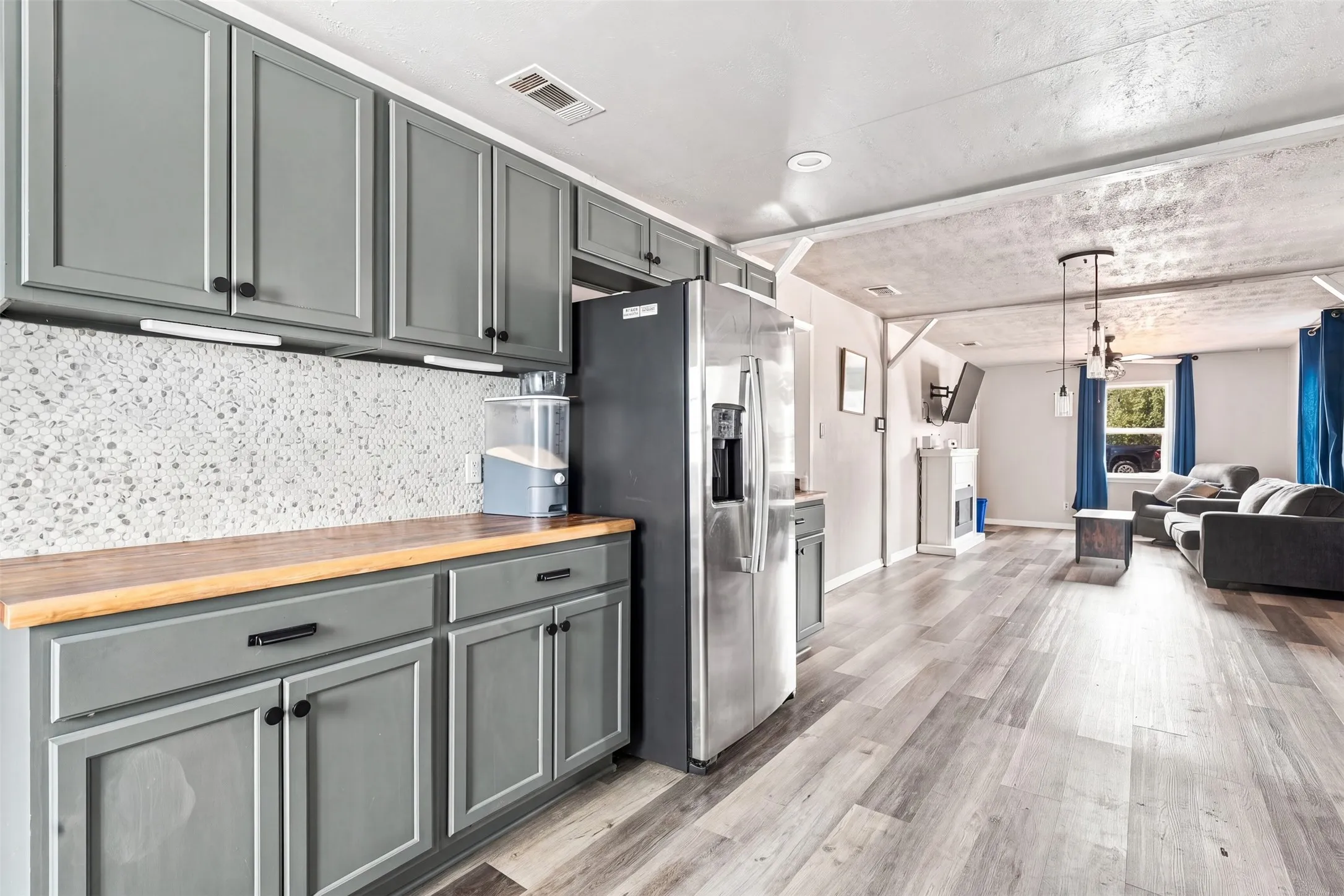 Gray cabinetry with black hardware, wood-finish countertops, mosaic tile backsplash, and stainless steel refrigerator