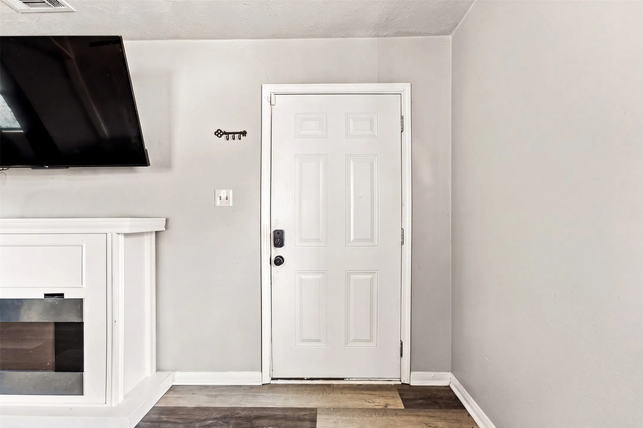 White paneled door with dark hardware, light gray wall finish, and multi-tone wood-finish flooring