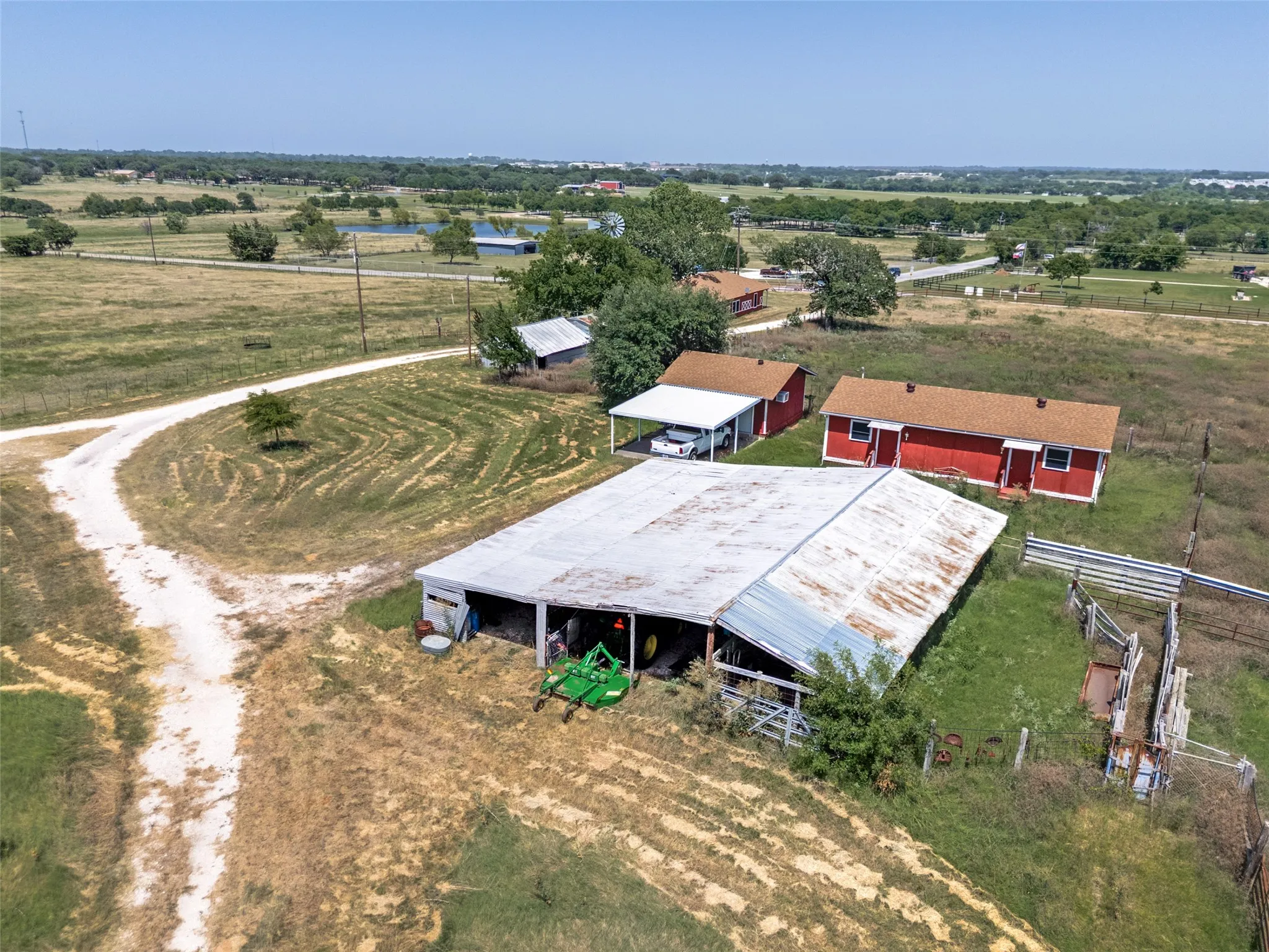 Gravel driveway with multiple structures, including a red building, a carport, and a metal-roofed barn