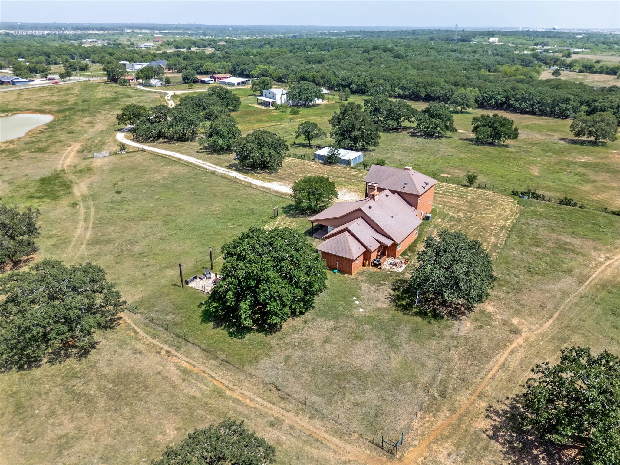 Brick exterior home with a gabled roof, surrounded by mature trees and expansive green space