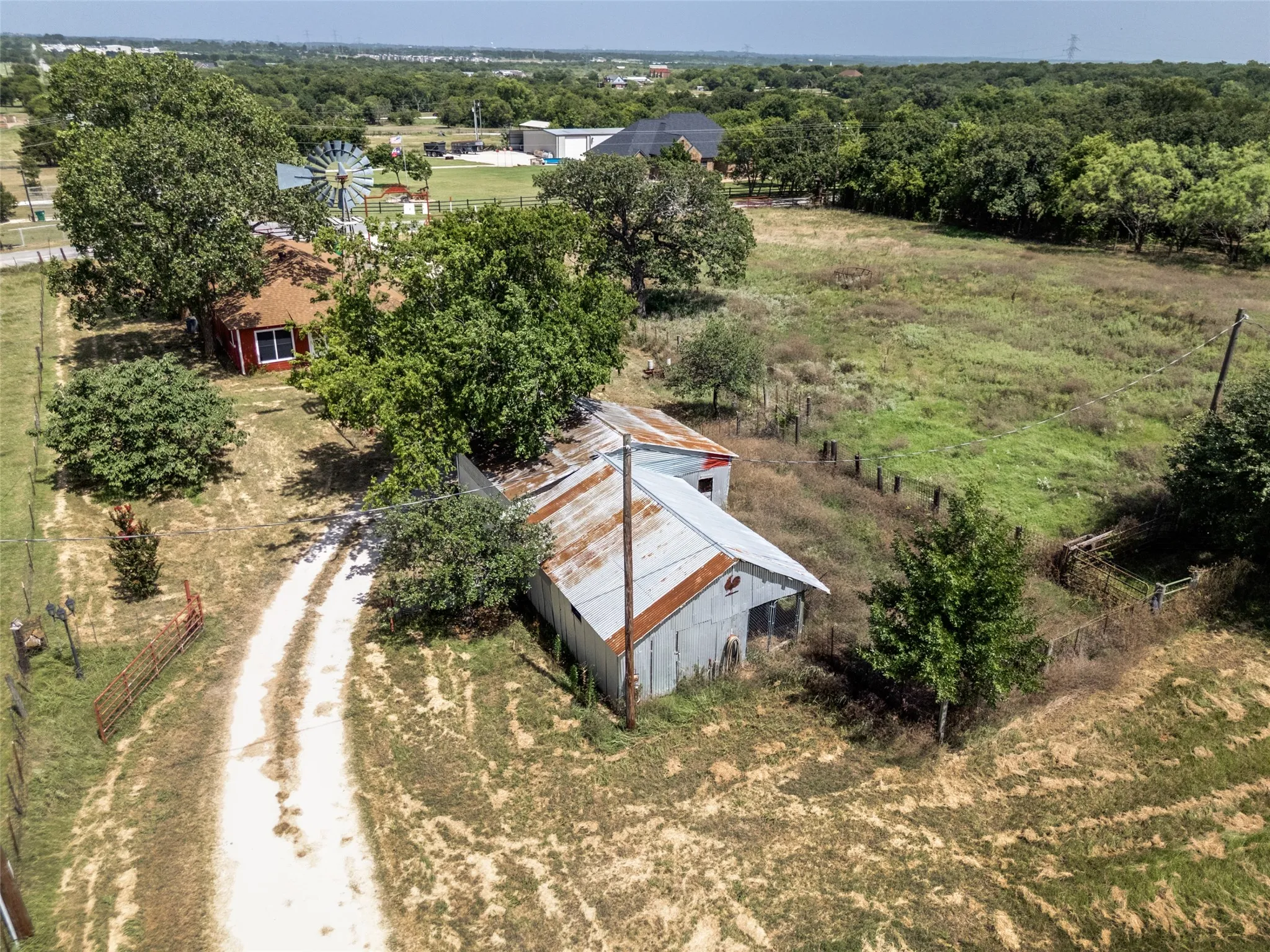 Expansive rural property featuring a red-sided structure with a red roof, a separate corrugated metal building, a dirt drive, and a windmill