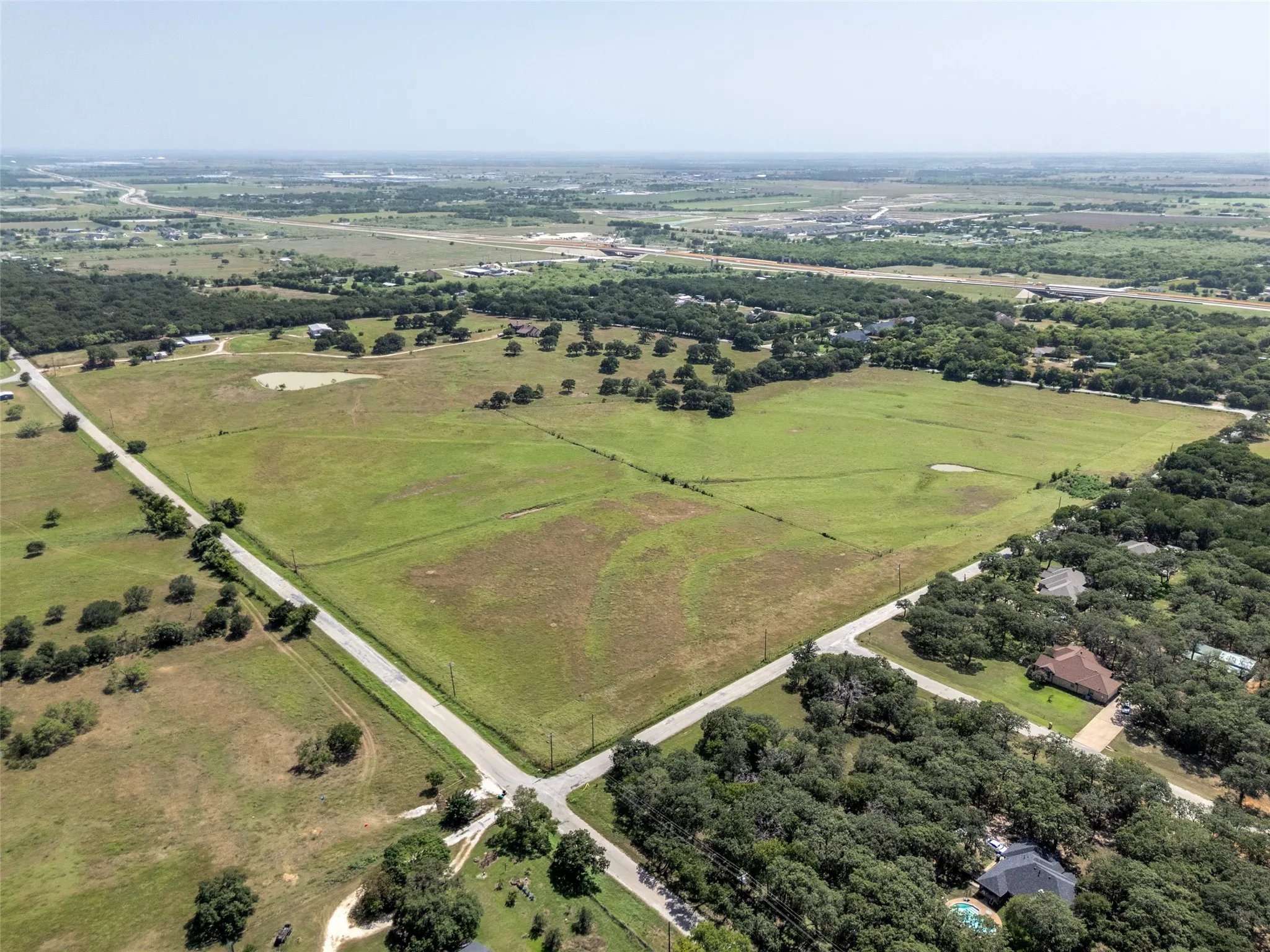 Expansive land parcel featuring a natural pond, established perimeter fencing, and mature trees