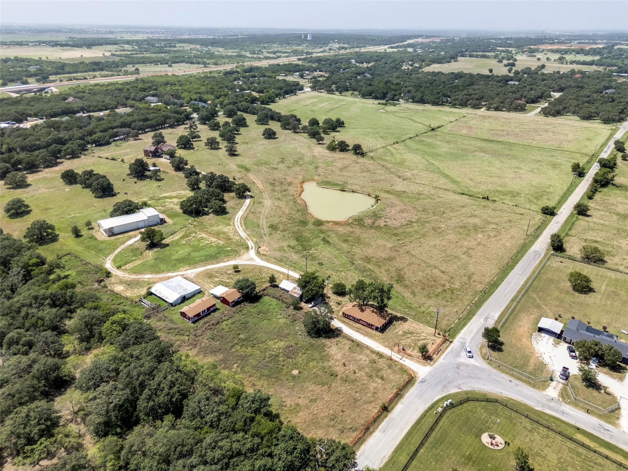 Expansive property featuring a private pond, multiple outbuildings, and a main residence with a brown roof