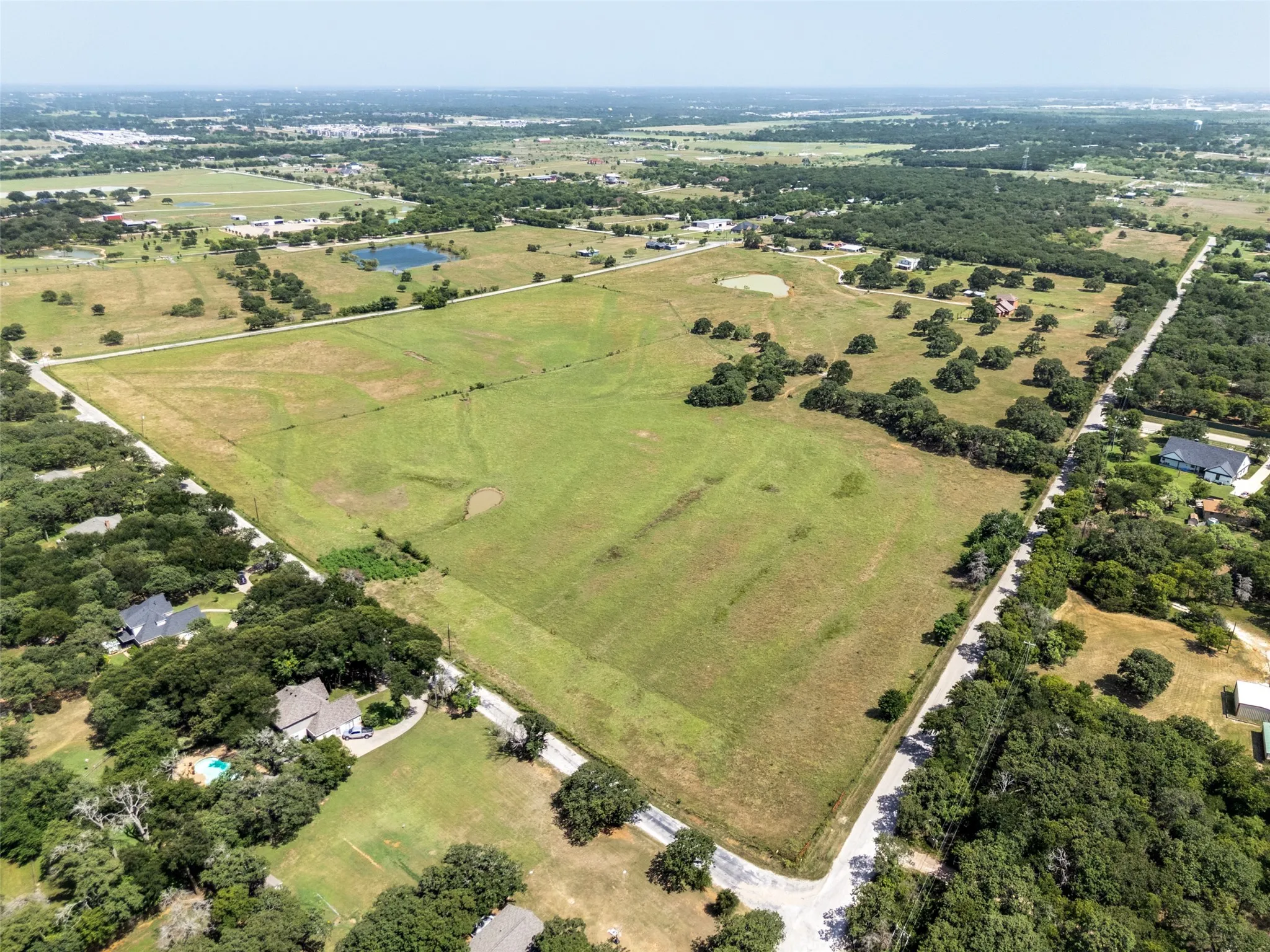 Expansive land parcel featuring open fields, scattered mature trees, and a visible pond