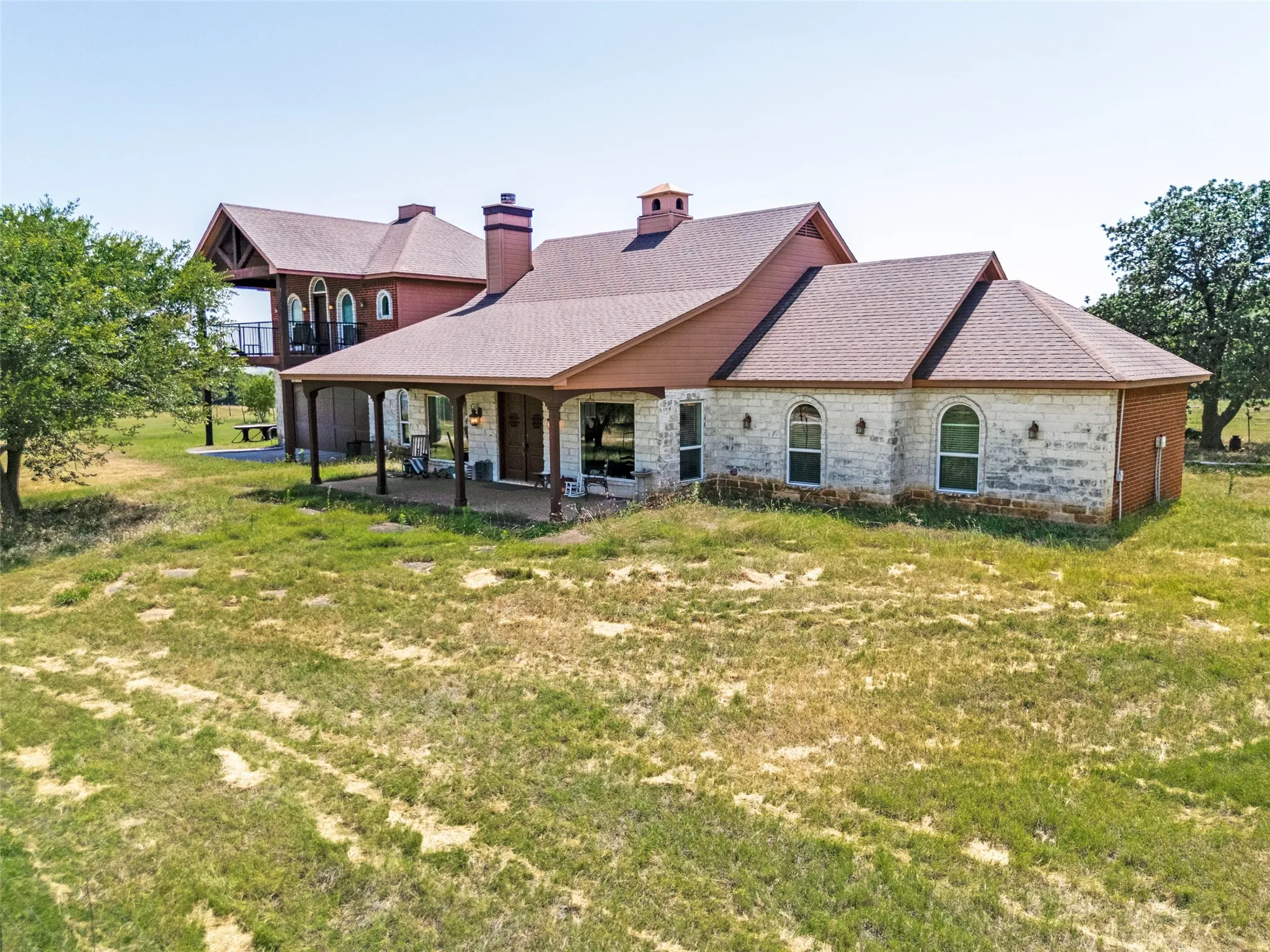 Stone and brick exterior with arched windows, covered porch, multiple gables, and a second-story balcony