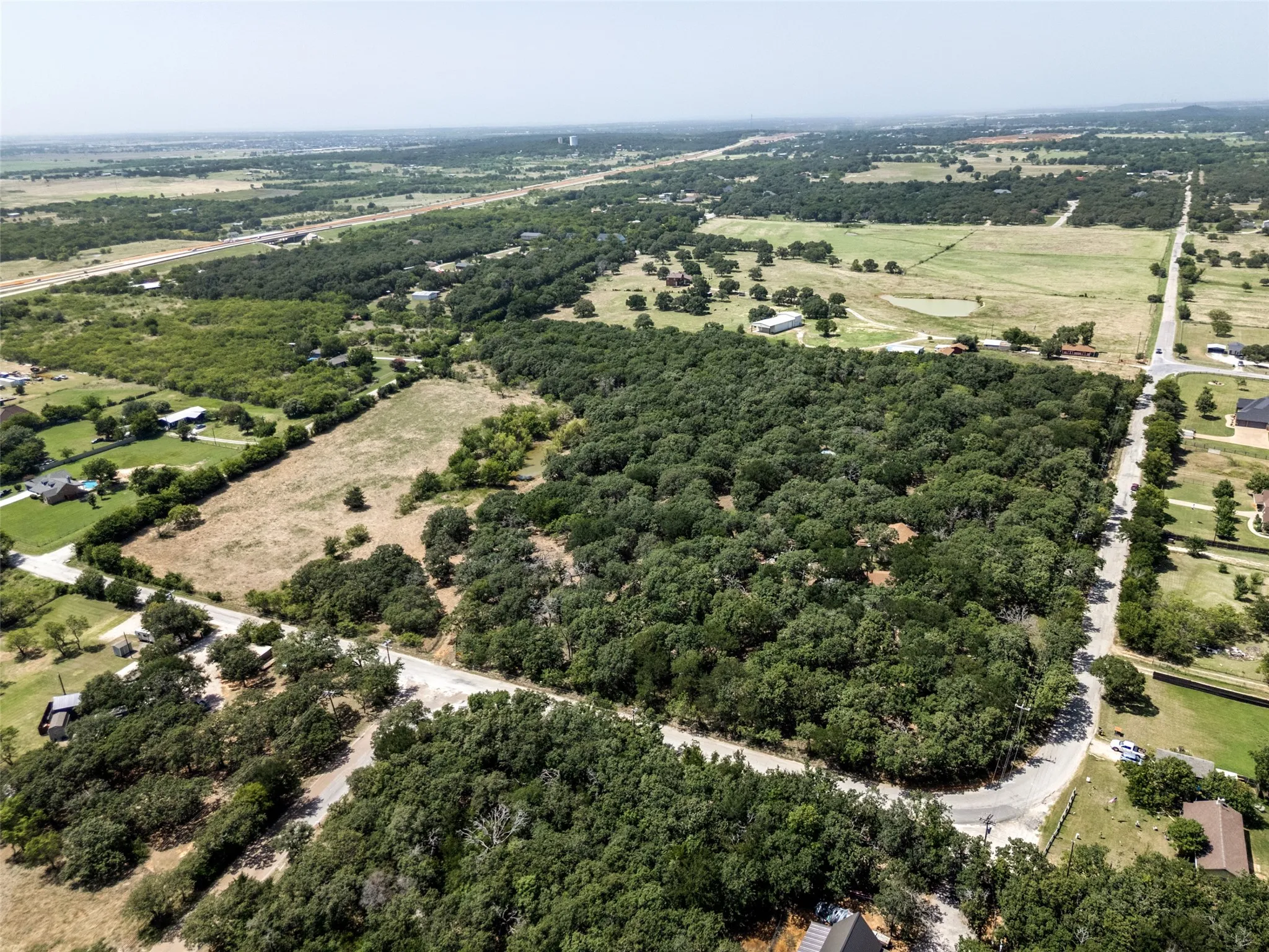 Expansive wooded land featuring mature trees, a paved road, and surrounding rural properties